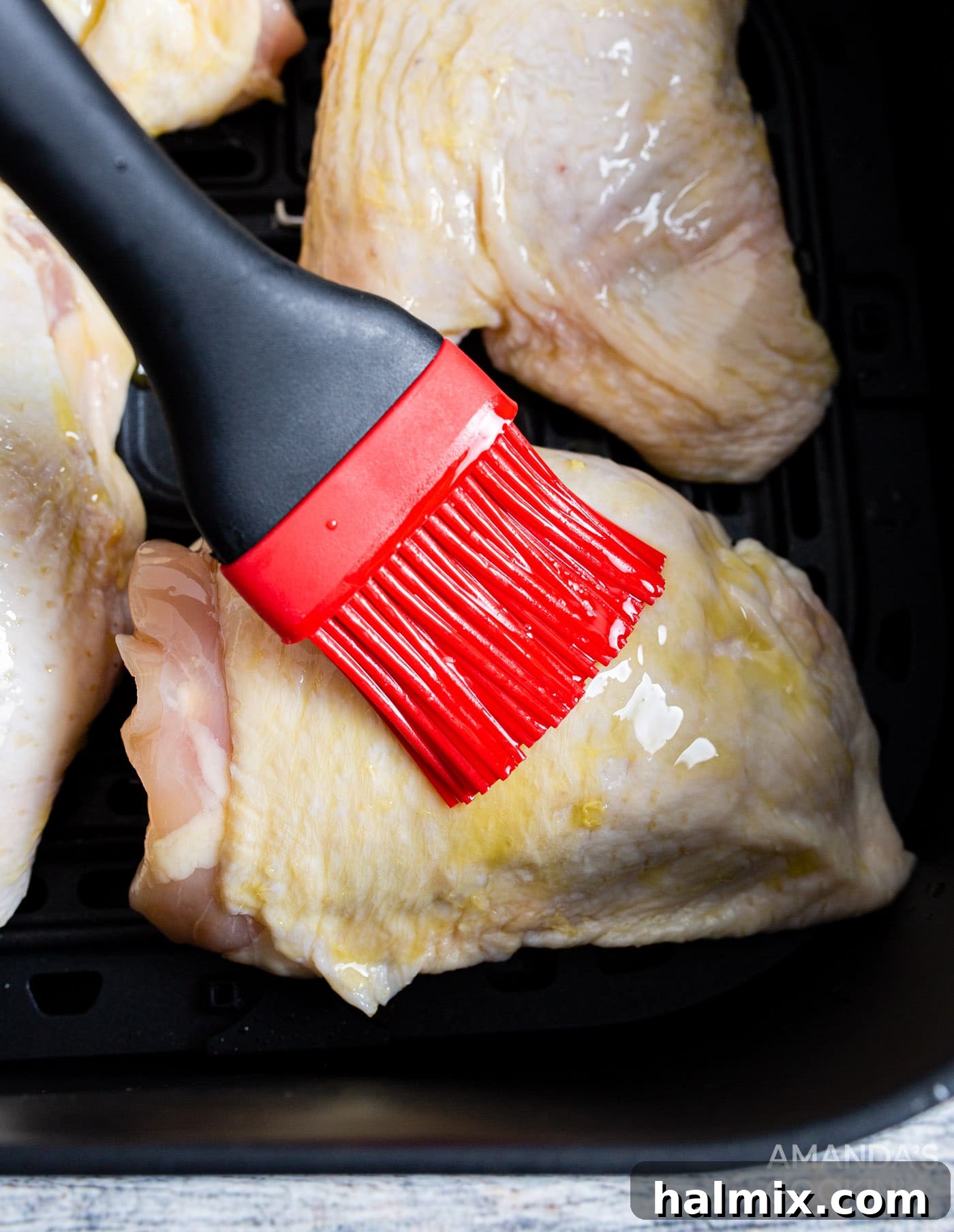 Golden Crispy Air Fryer Thighs 6 close-up shot of a hand brushing olive oil onto a raw chicken thigh before seasoning