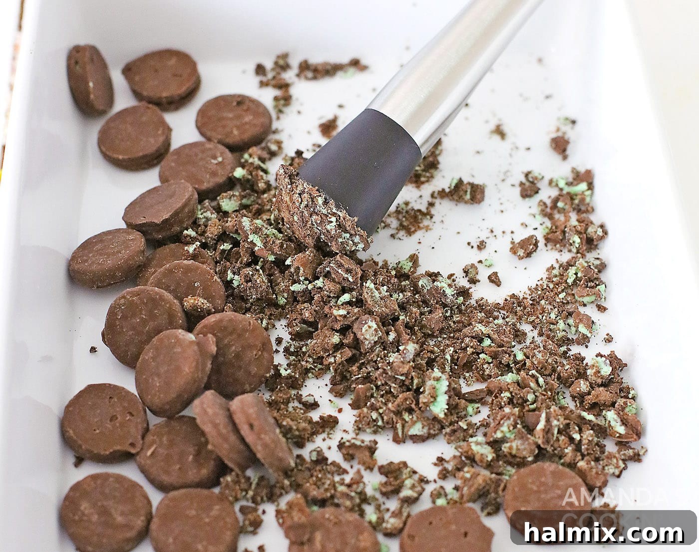 Crushing Oreo Thin Mint cookies into fine crumbs in a shallow dish, preparing them for the shot glass rims.