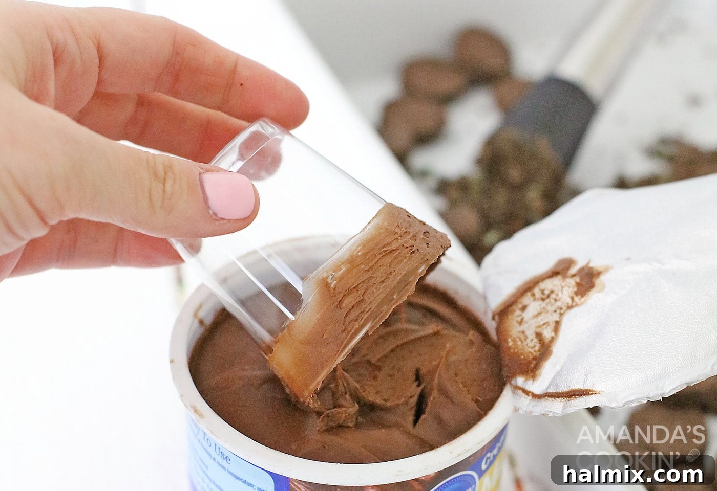 Coating the rim of a shot glass evenly with chocolate frosting to create a sticky base for the cookie crumbs.