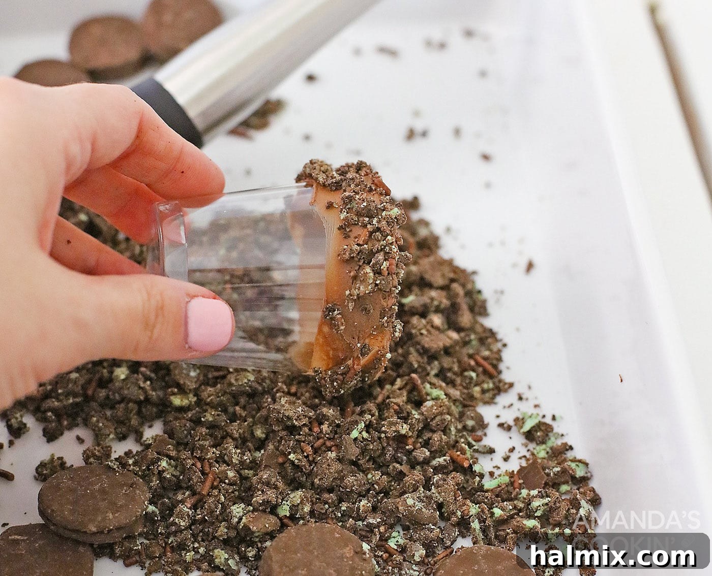 Rolling the frosting-coated rim of a shot glass in crushed mint cookies for a festive and delicious decoration.