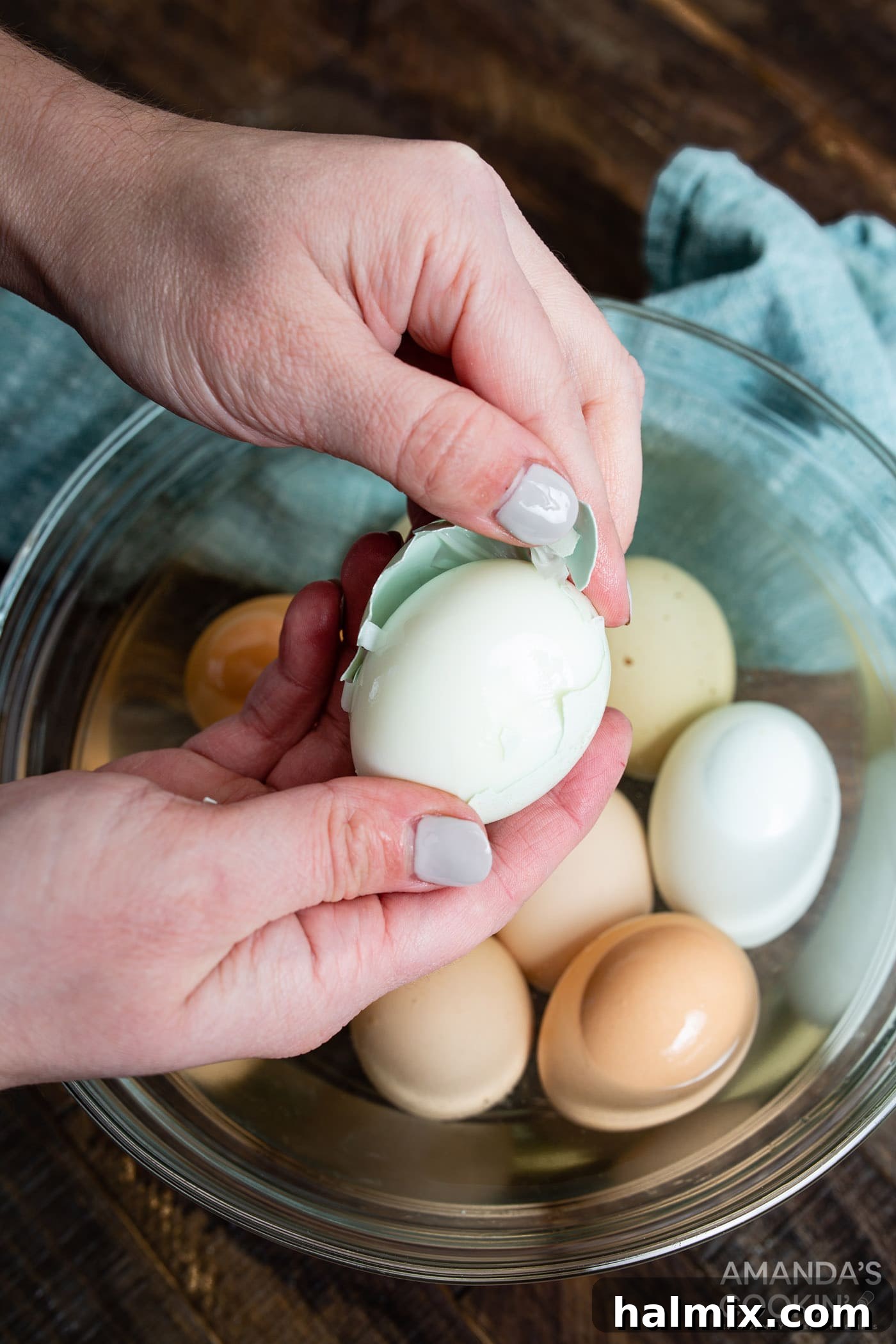 hands peeling a hard boiled egg, showing the smooth white surface beneath