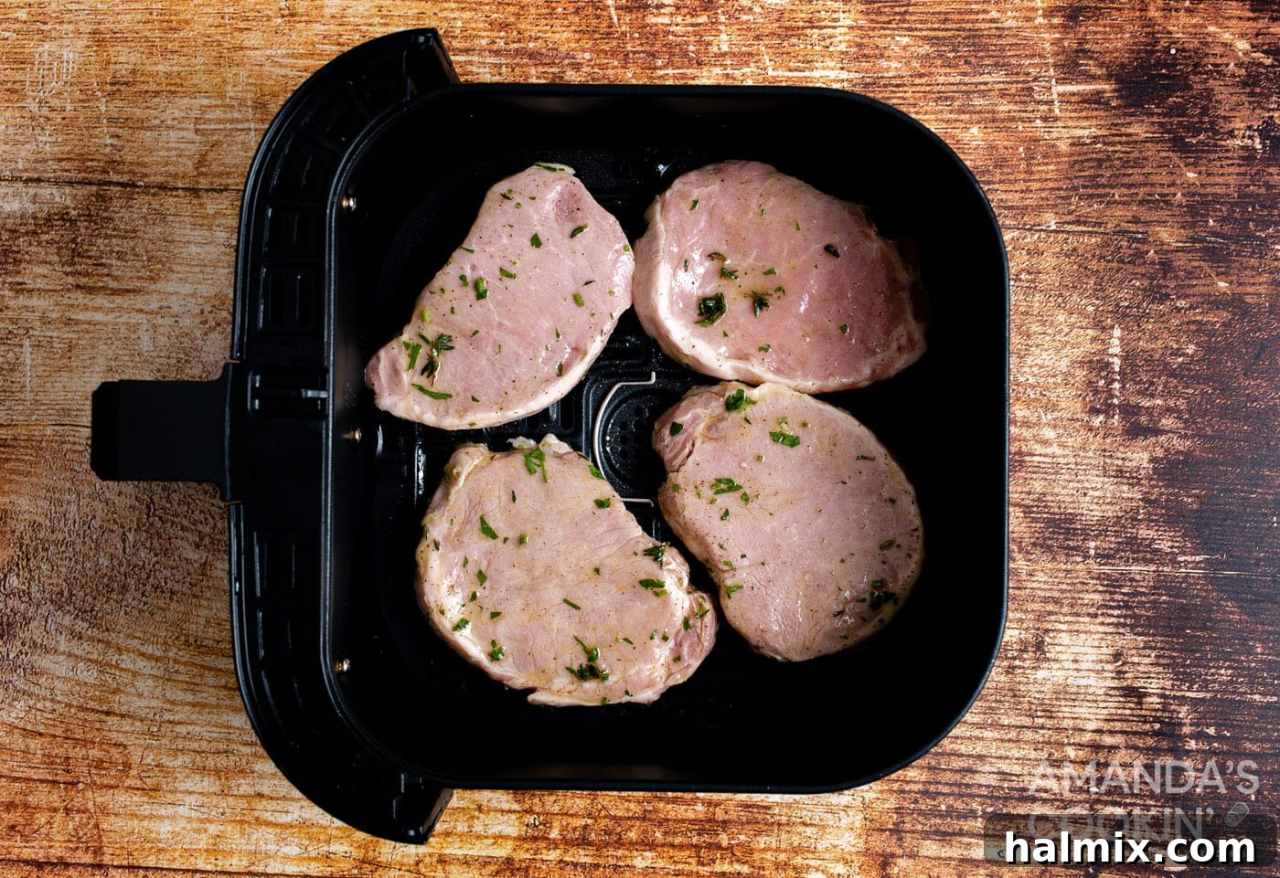 Pork chops cooking inside the air fryer basket, halfway through