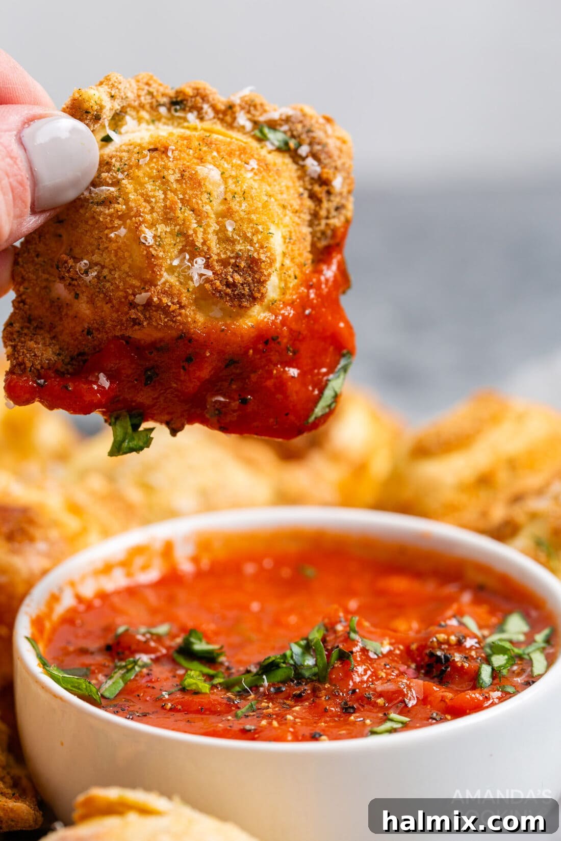 Crispy Golden Air Fryer Ravioli 11 Hand dipping a golden-brown air fryer ravioli into a bowl of marinara sauce.
