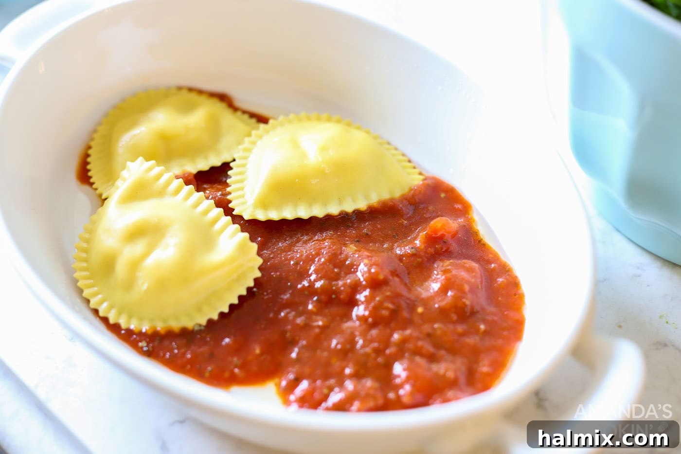 First layer of ravioli placed over marinara sauce in a baking dish.