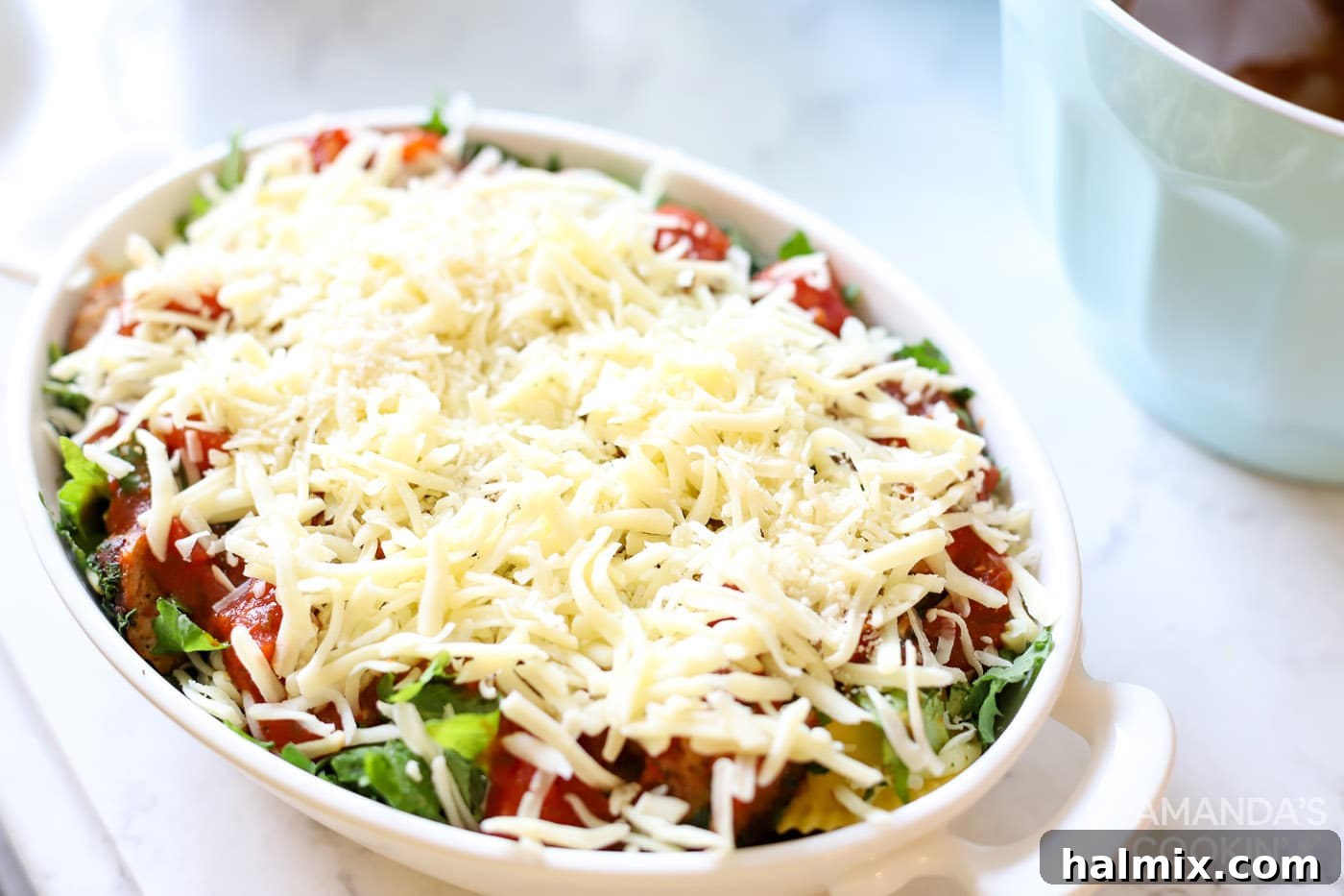 Shredded mozzarella cheese generously sprinkled on top of spinach and sauce in a dish, ready for baking.