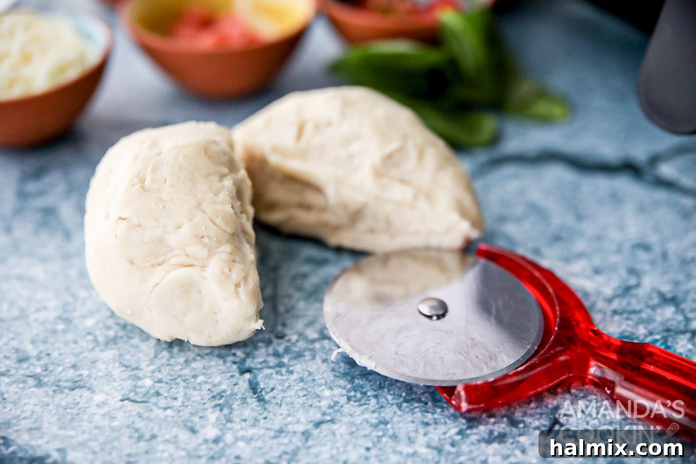 Pizza dough ball cut precisely in half, ready for shaping into individual crusts.