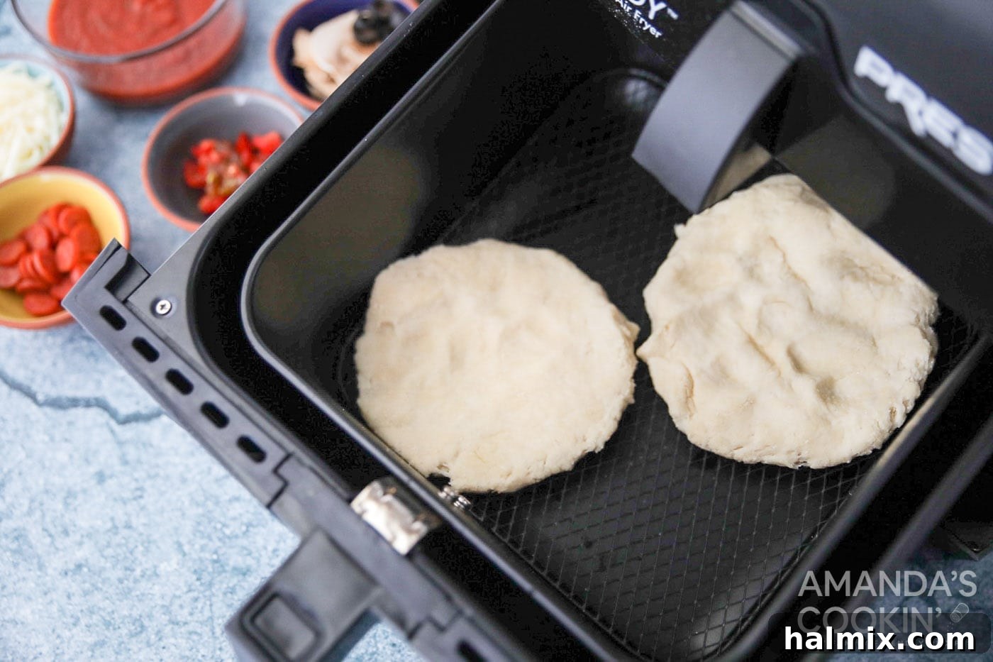 Two perfectly shaped pizza dough circles placed side-by-side inside an air fryer basket, ready for toppings.