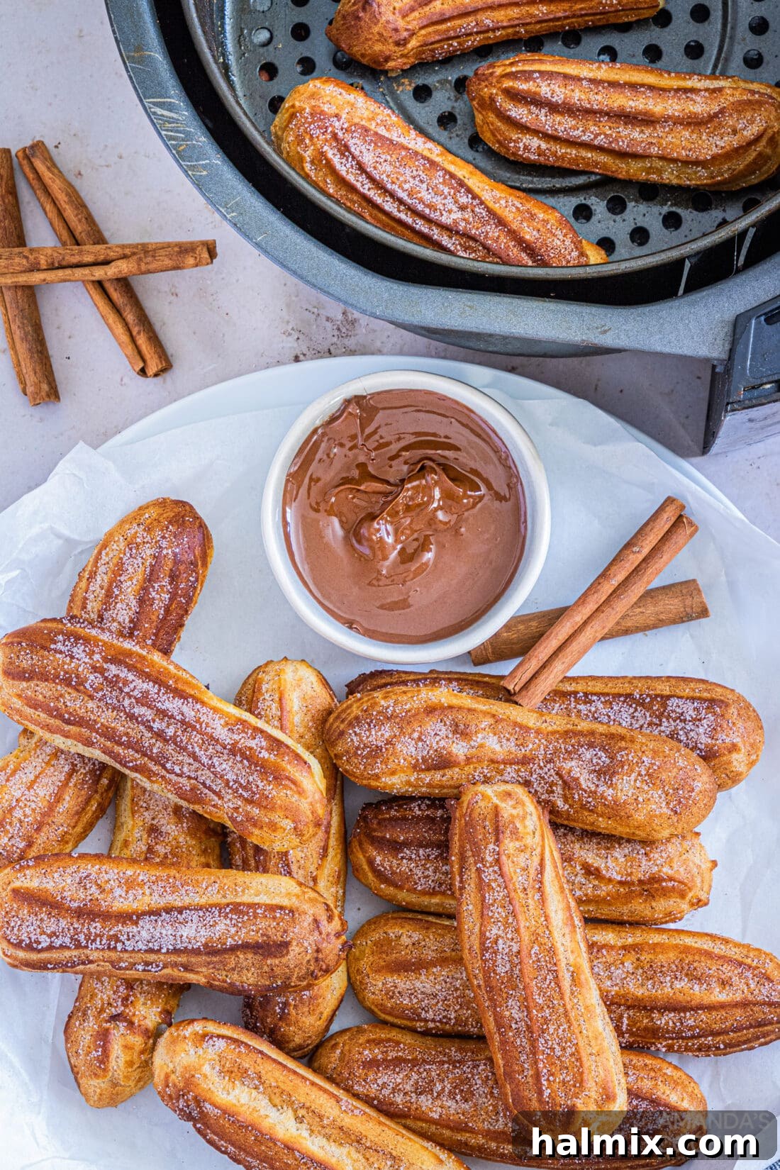 plate of Air Fryer Churros sitting by an air fryer basket with more churros