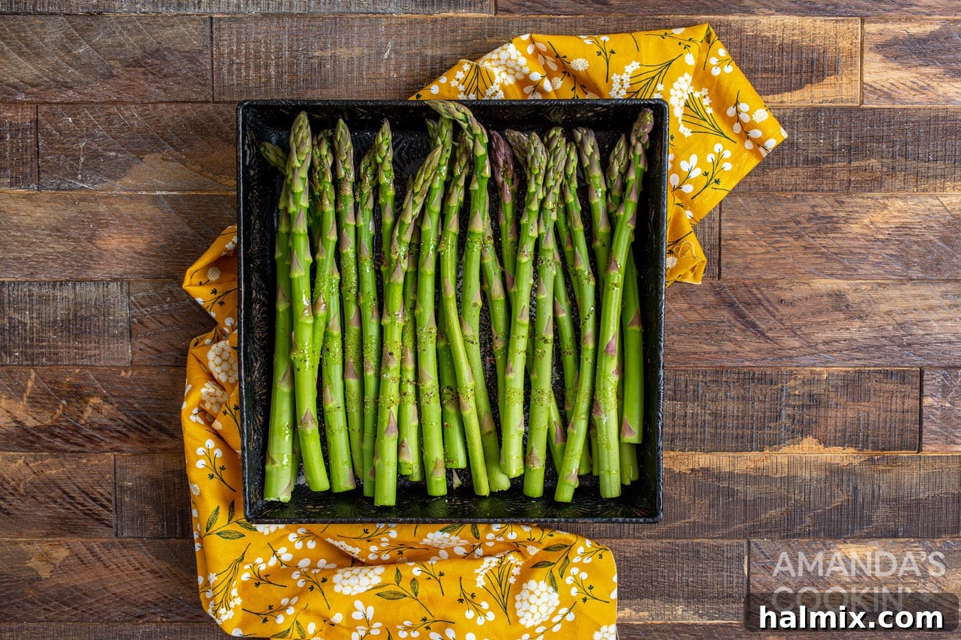 asparagus in a casserole dish being tossed with olive oil, salt, and pepper