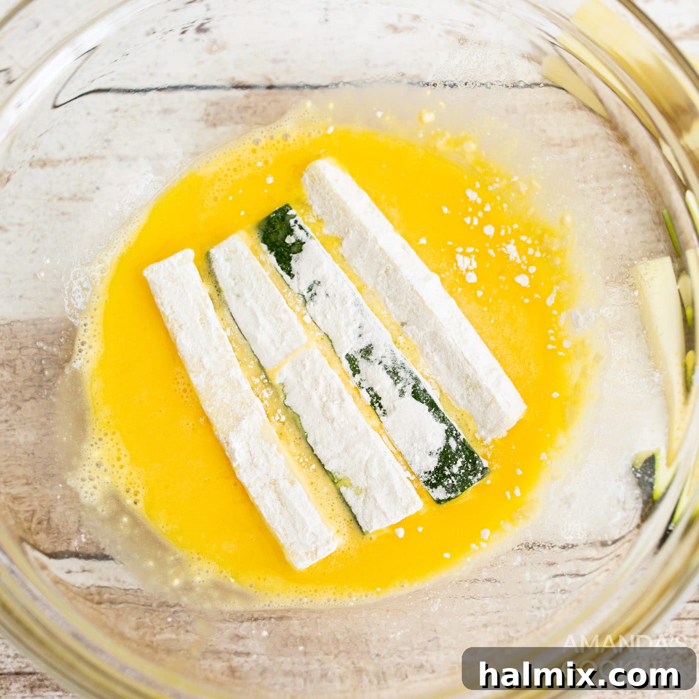 Dredging flour-coated zucchini sticks in eggwash