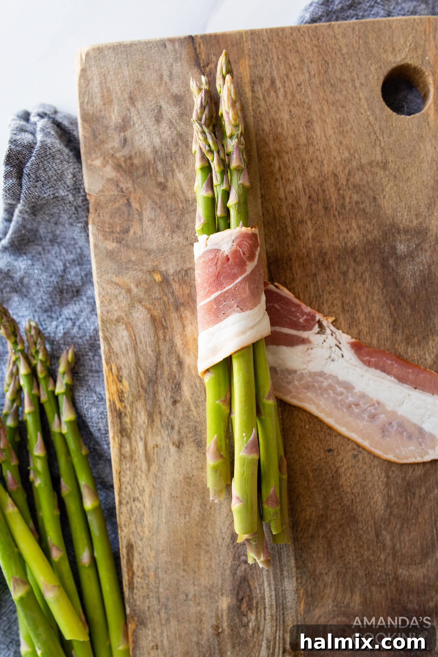 Bacon being carefully wrapped around a bundle of asparagus spears