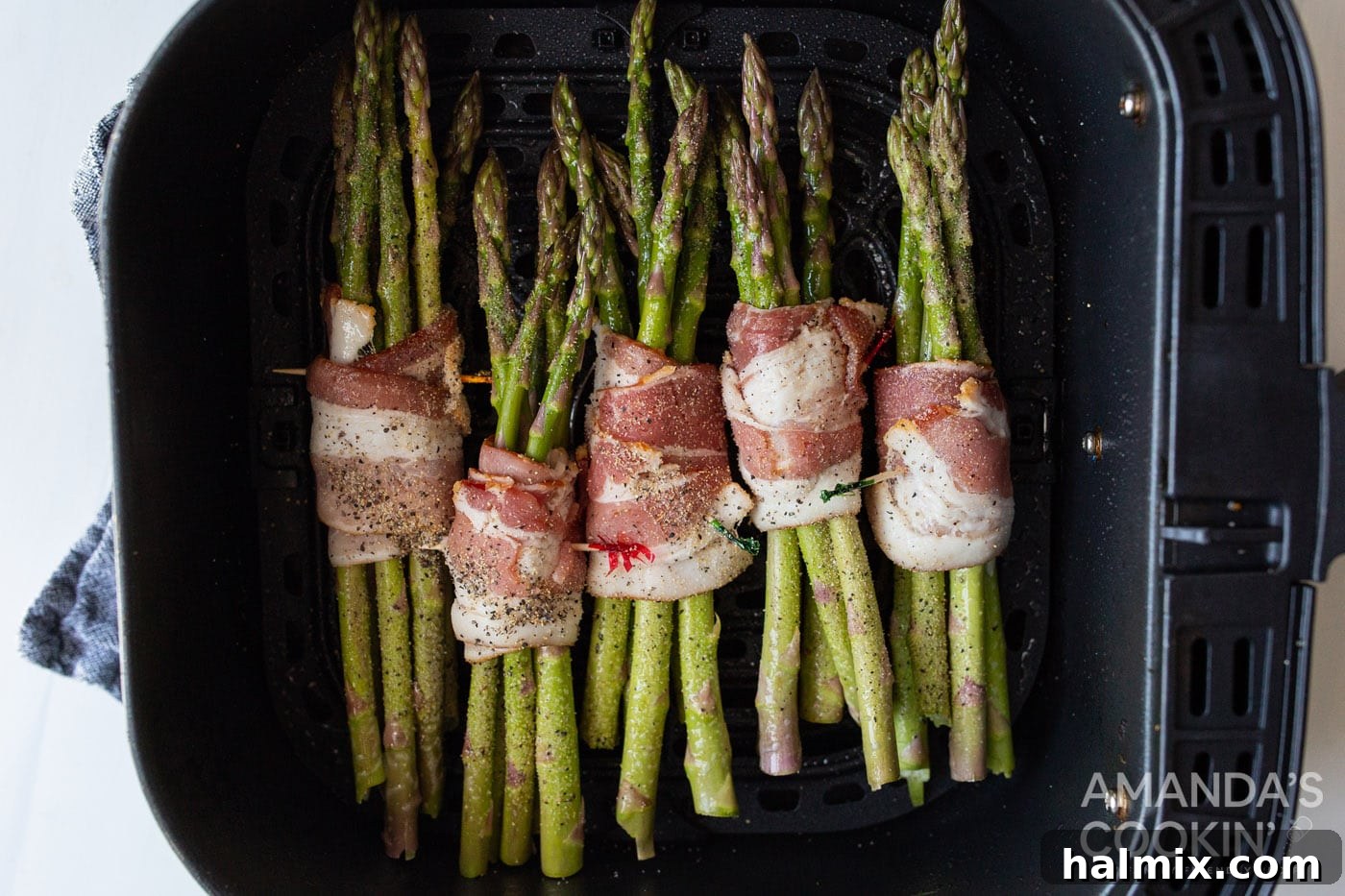 Bacon wrapped asparagus bundles placed in a grate-lined air fryer basket