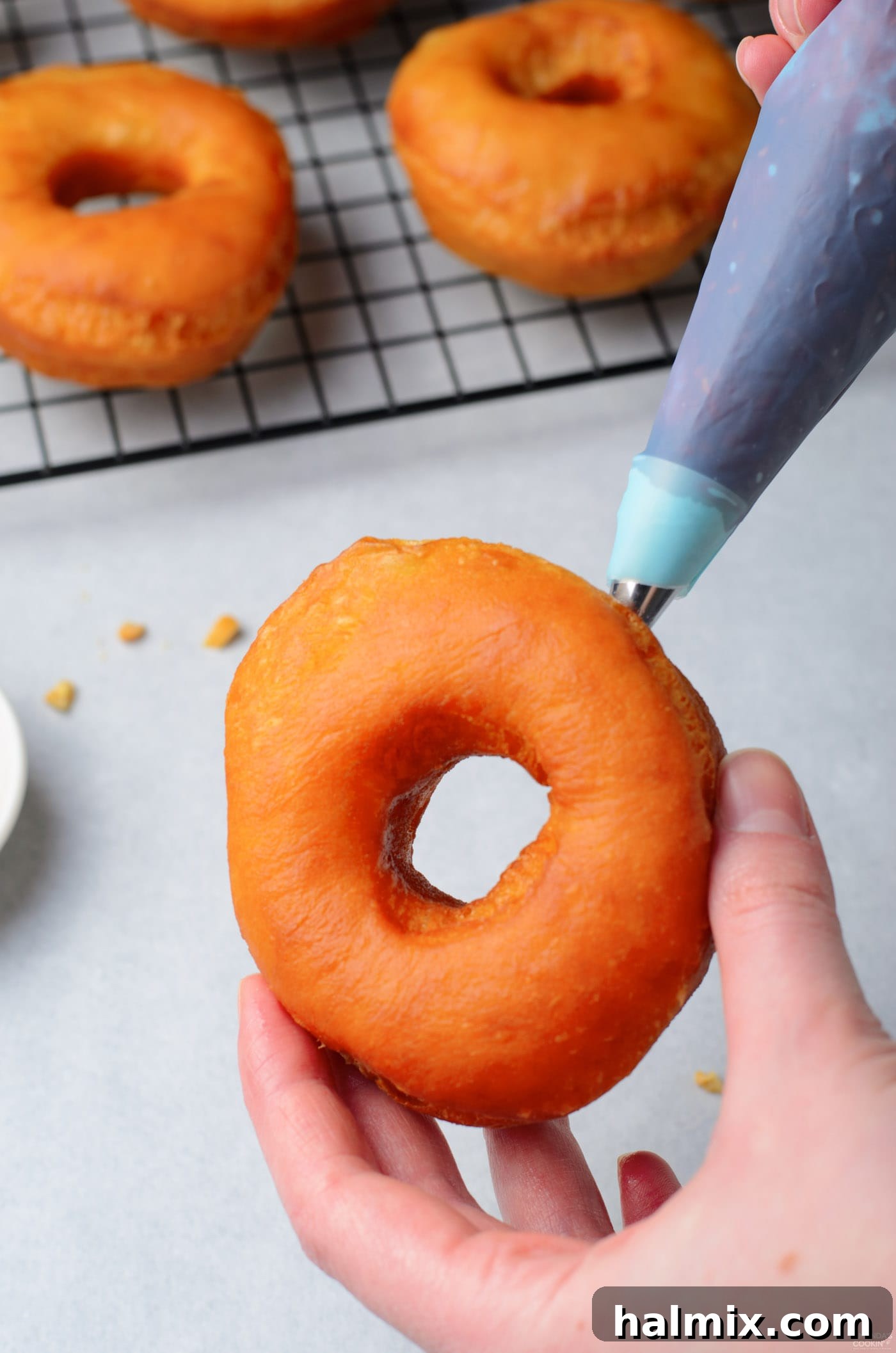 A pastry bag carefully injecting bright red jelly into the side of a freshly fried donut.