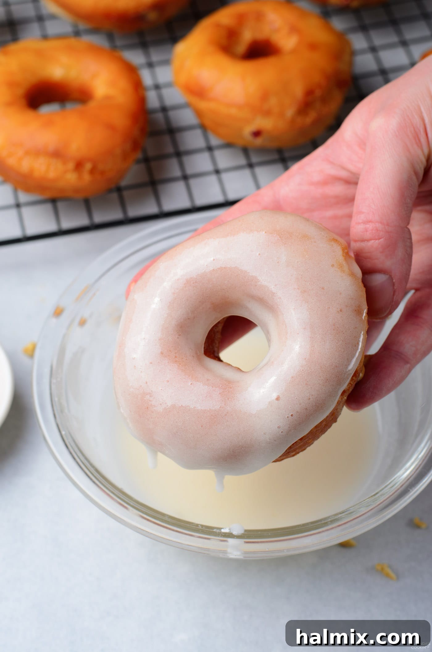 A donut being dipped into a sweet, white glaze, ready for topping.