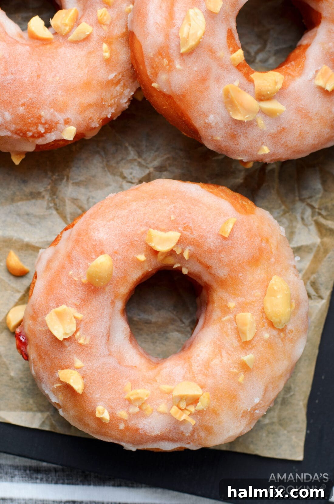 An inviting overhead view of a single glazed peanut butter and jelly donut, topped with chopped peanuts.