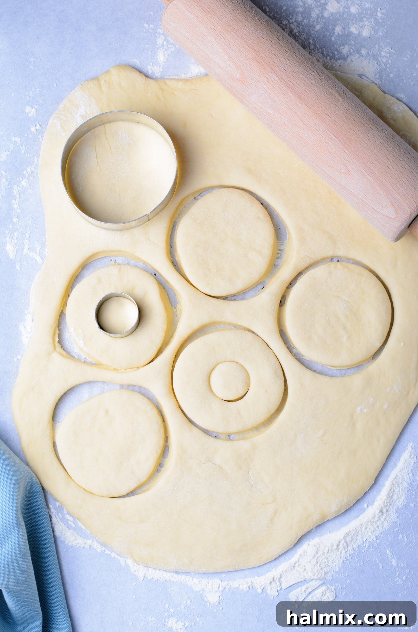 Round donut shapes being cut from rolled-out dough using a specialized donut cutter.
