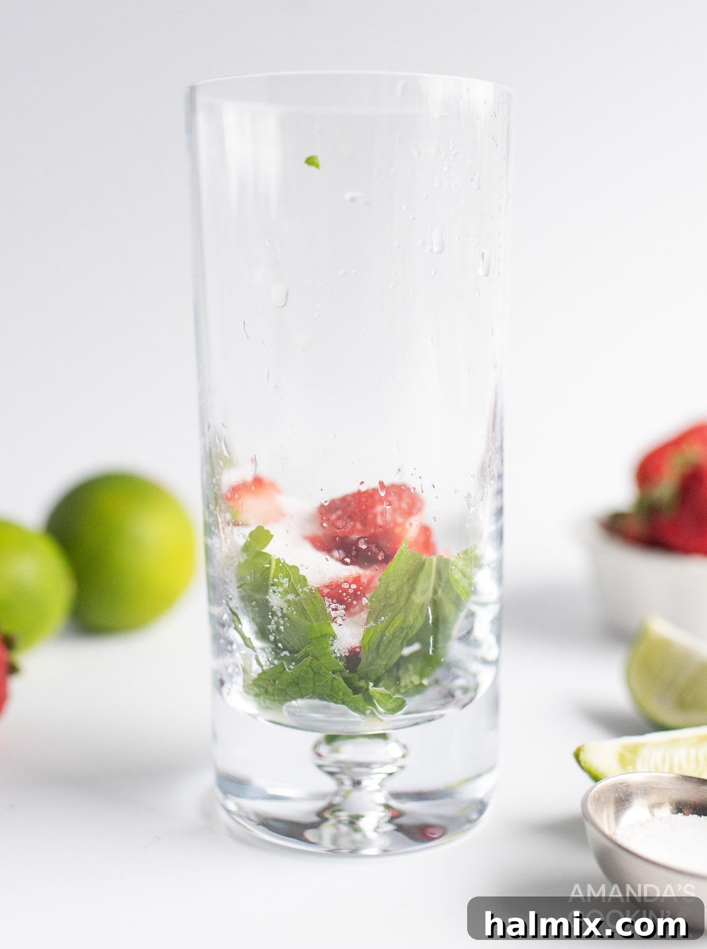 Mint leaves and sliced strawberries being gently muddled in a highball glass