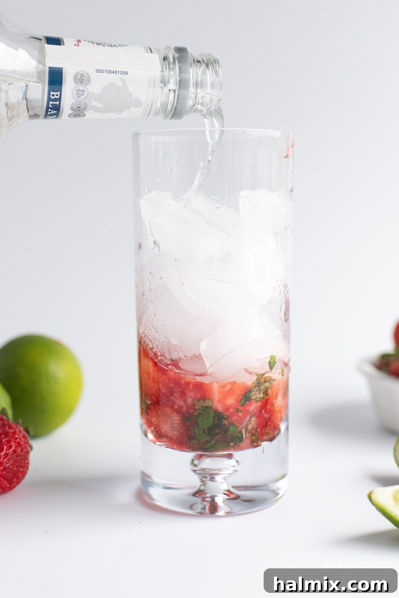 Pouring chilled club soda over ice, rum, muddled strawberries, and mint in a highball glass