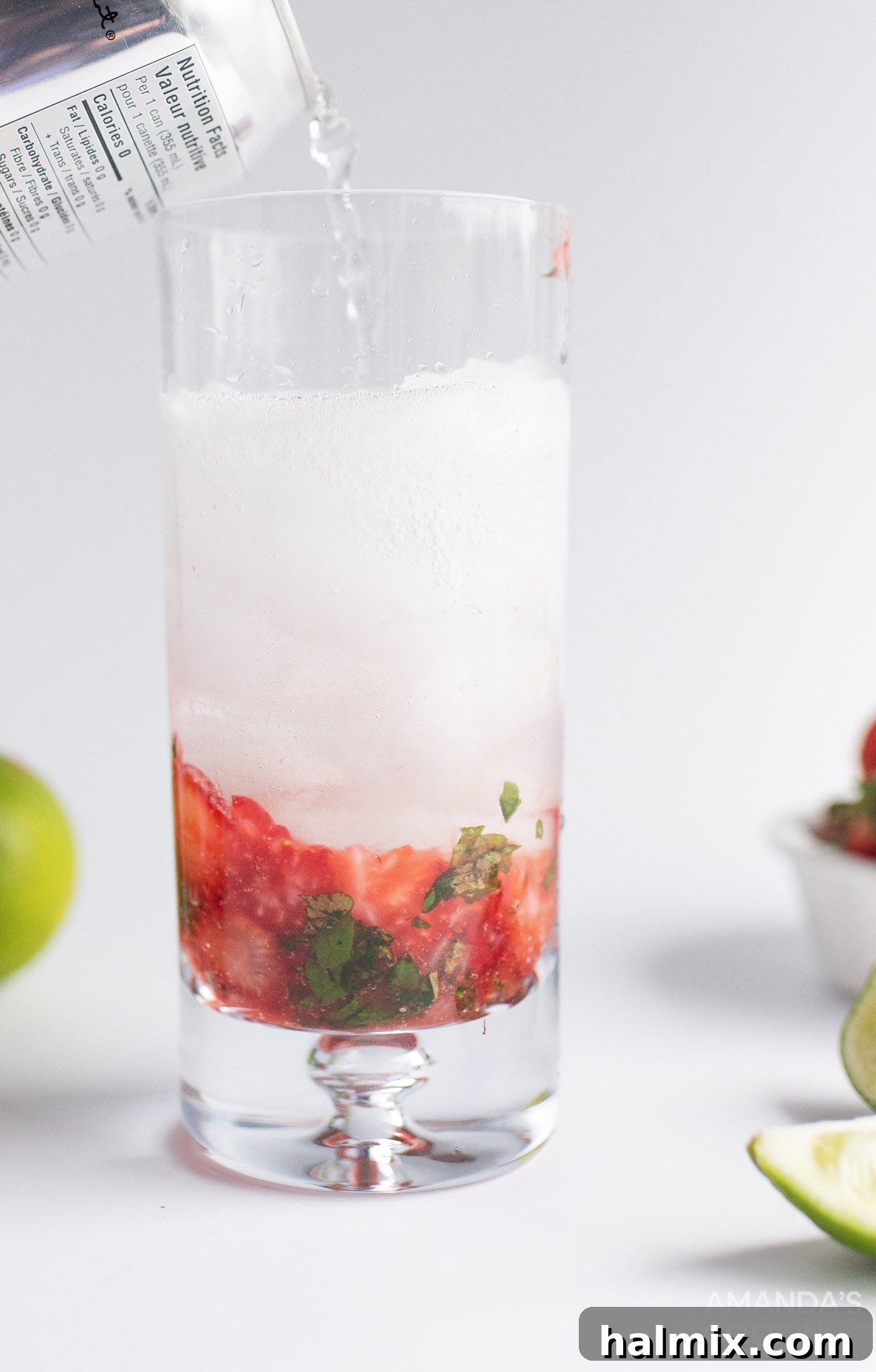 A finished Strawberry Mojito being stirred, garnished with lime and strawberry