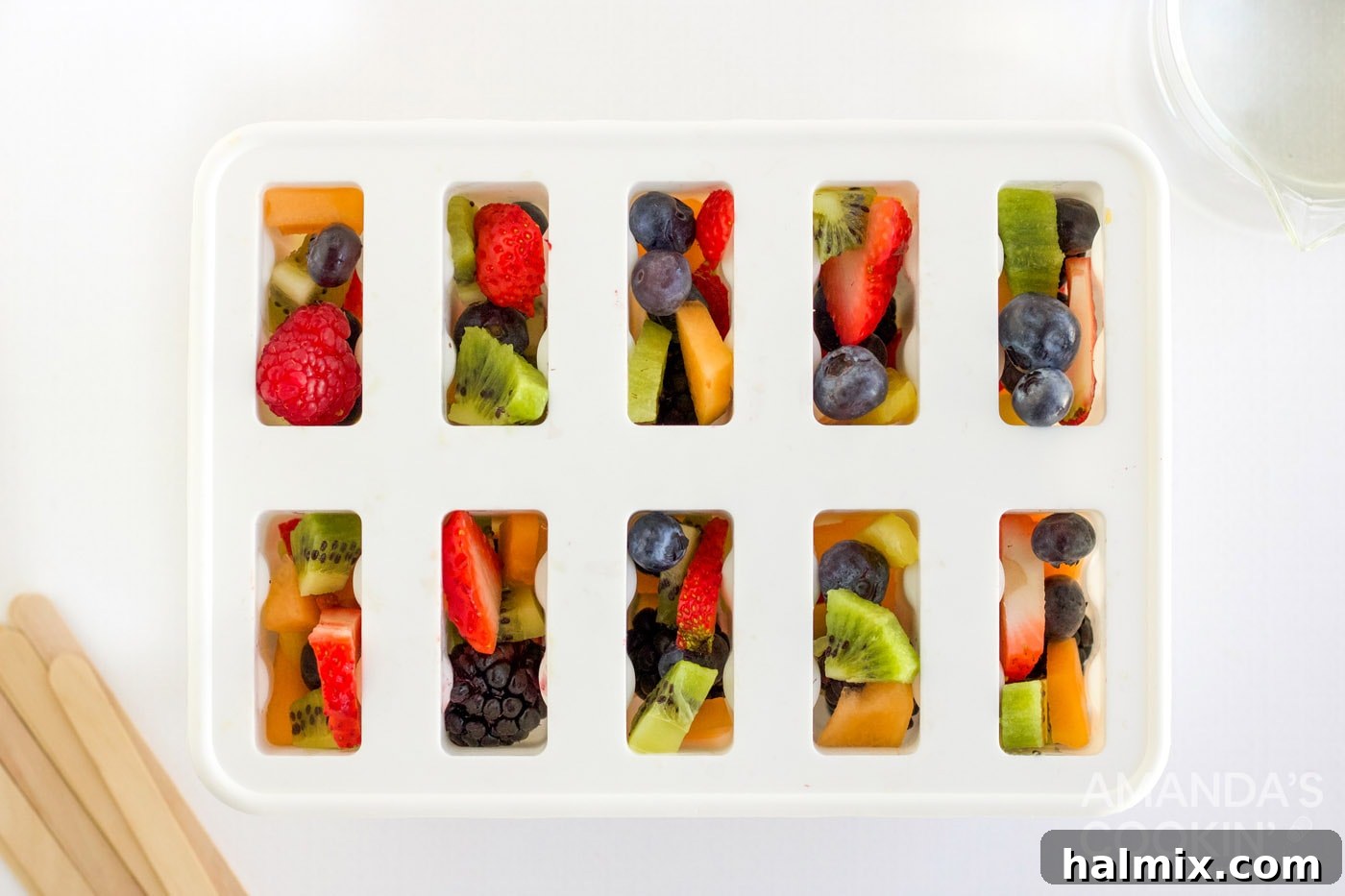 Hands carefully placing chopped fruit into a clear popsicle mold