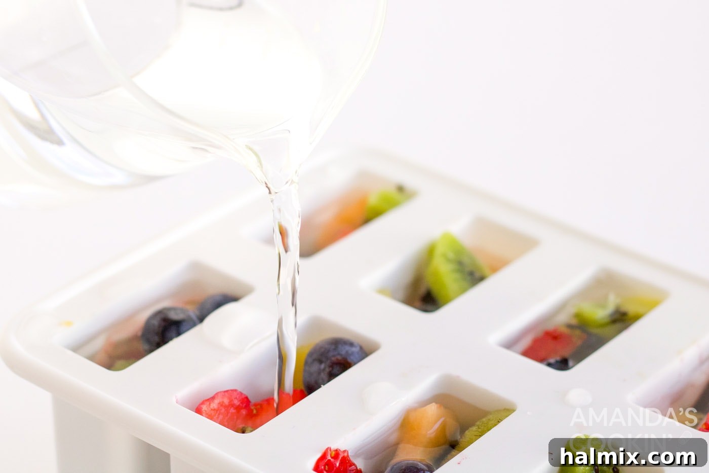 Pouring clear white grape juice over a colorful mix of fruit in a popsicle mold