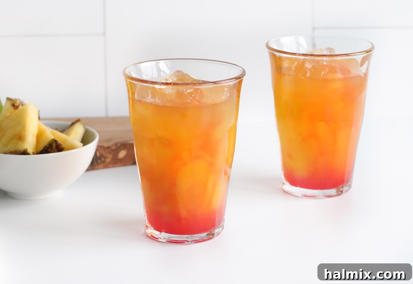 grenadine being poured into a glass already containing pineapple juice, mango juice, and rum, adding a vibrant red layer.