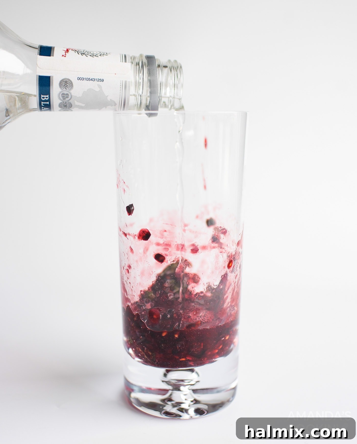 Midnight Mojito 6 A stream of clear white rum is being poured from a jigger into a tall glass containing freshly muddled blackberries and mint leaves, forming the cocktail base.