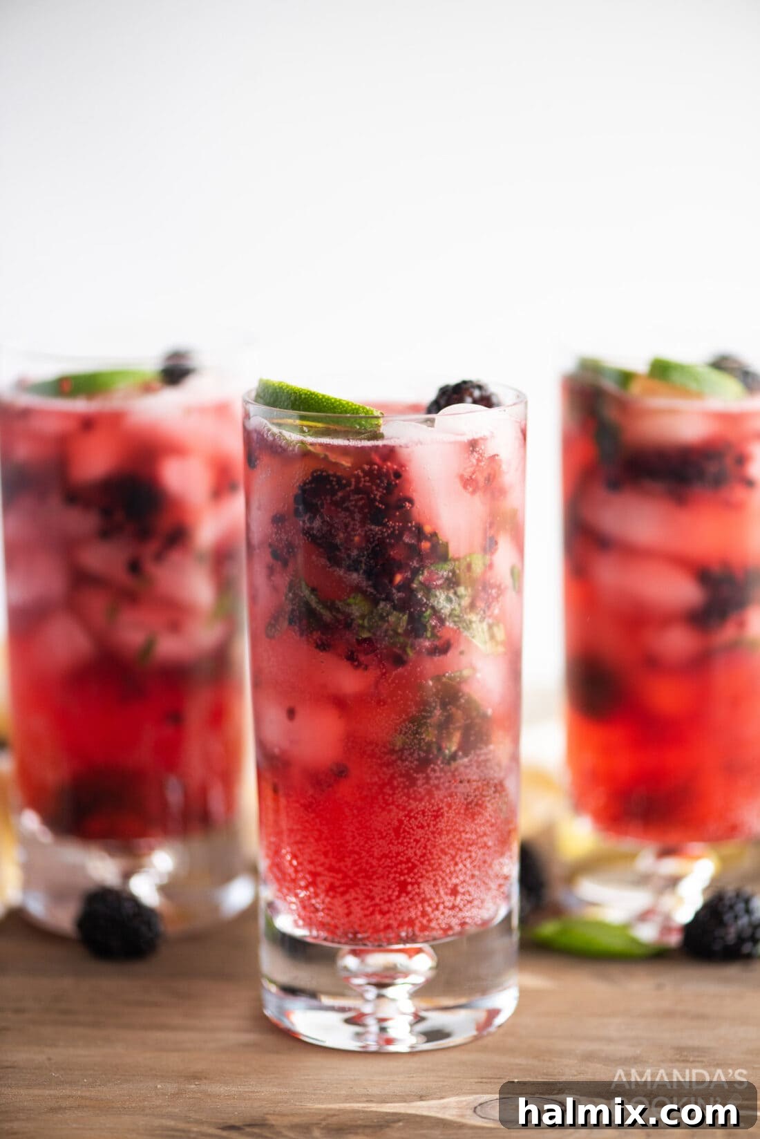 Midnight Mojito 8 Three perfectly prepared blackberry mojitos, each in a tall glass, beautifully garnished with fresh fruit and mint, resting invitingly on a rustic wooden surface.