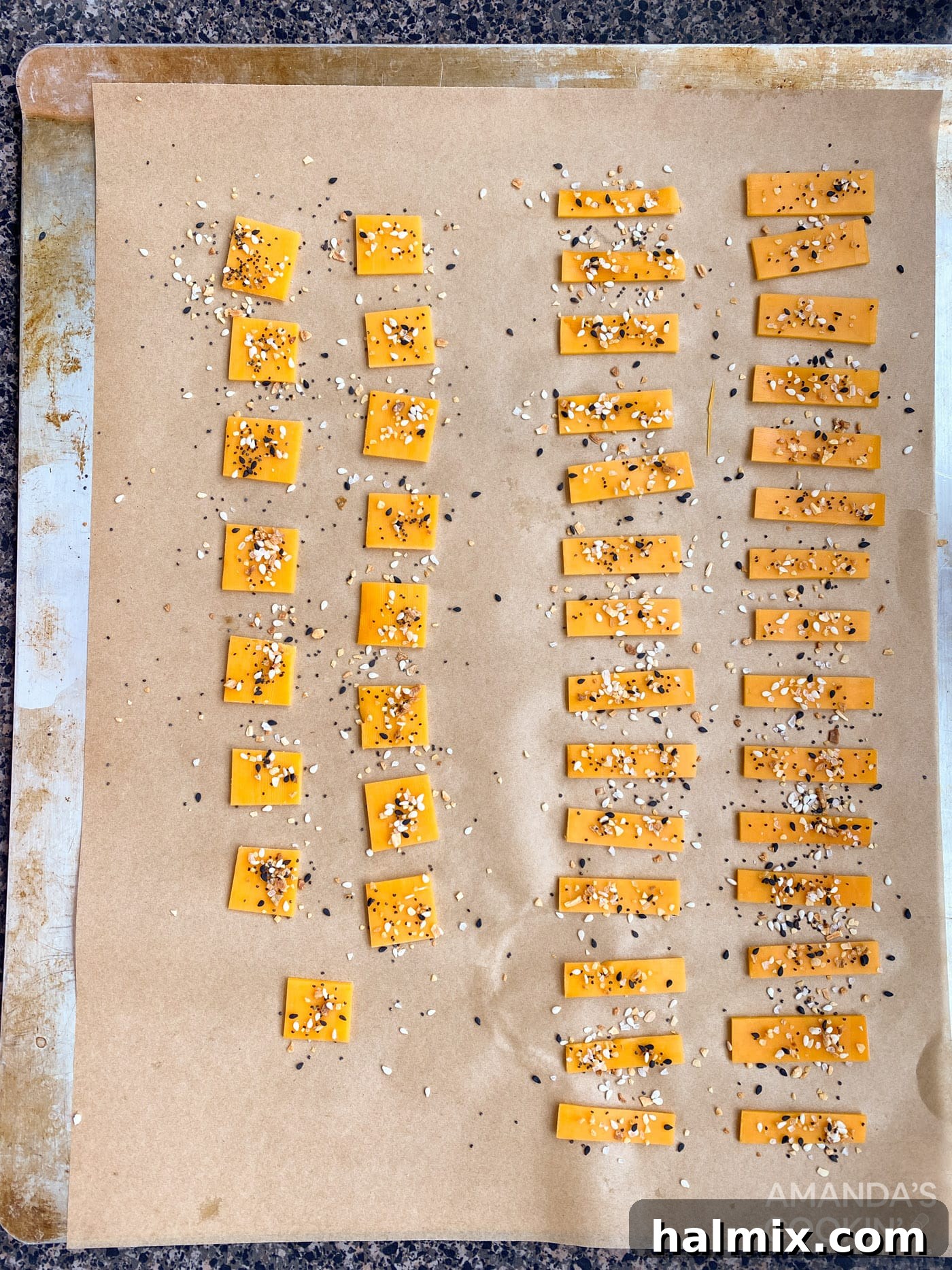Cheese pieces with Everything Bagel seasoning sprinkled on top, on a baking sheet.