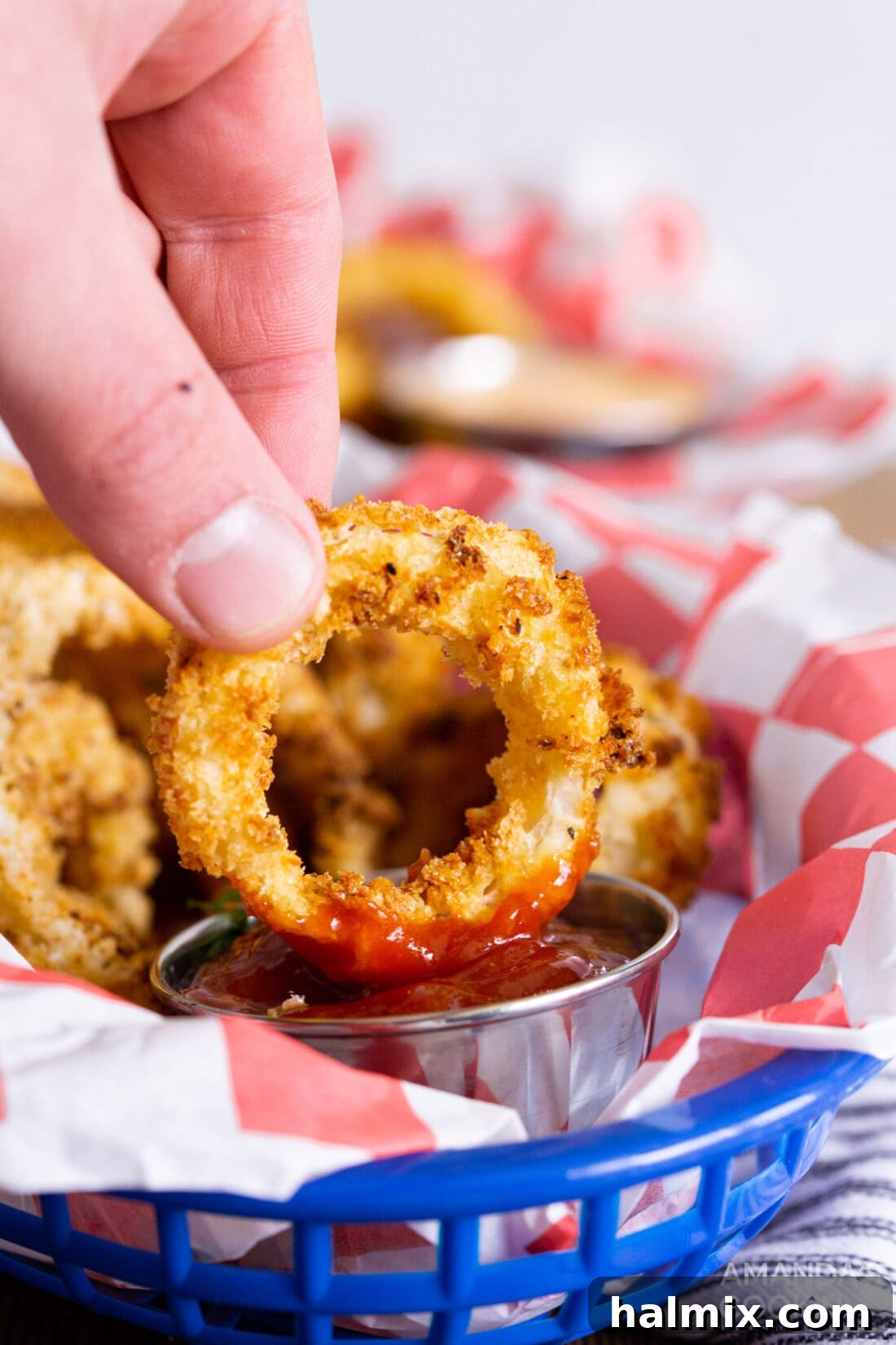 Golden Air-Fried Onion Rings 3 A hand dipping a crispy air fryer onion ring into a bowl of ketchup.