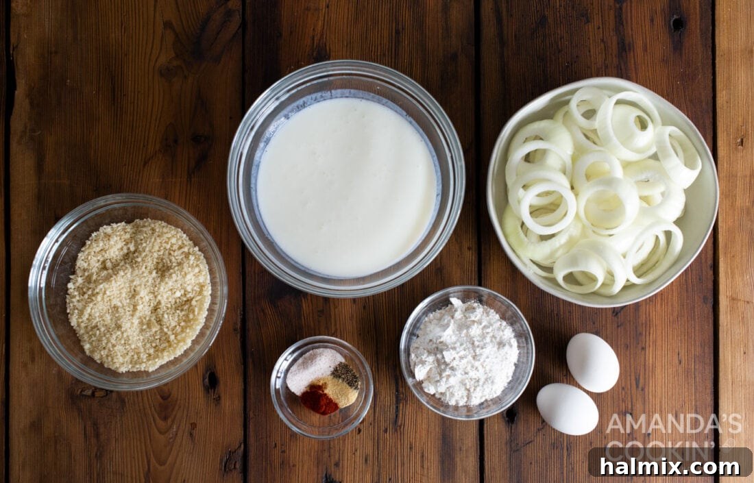 Golden Air-Fried Onion Rings 4 A flat lay photograph showcasing all the ingredients required for making Air Fryer Onion Rings, including a large yellow onion, buttermilk, flour, panko breadcrumbs, eggs, and various seasonings.