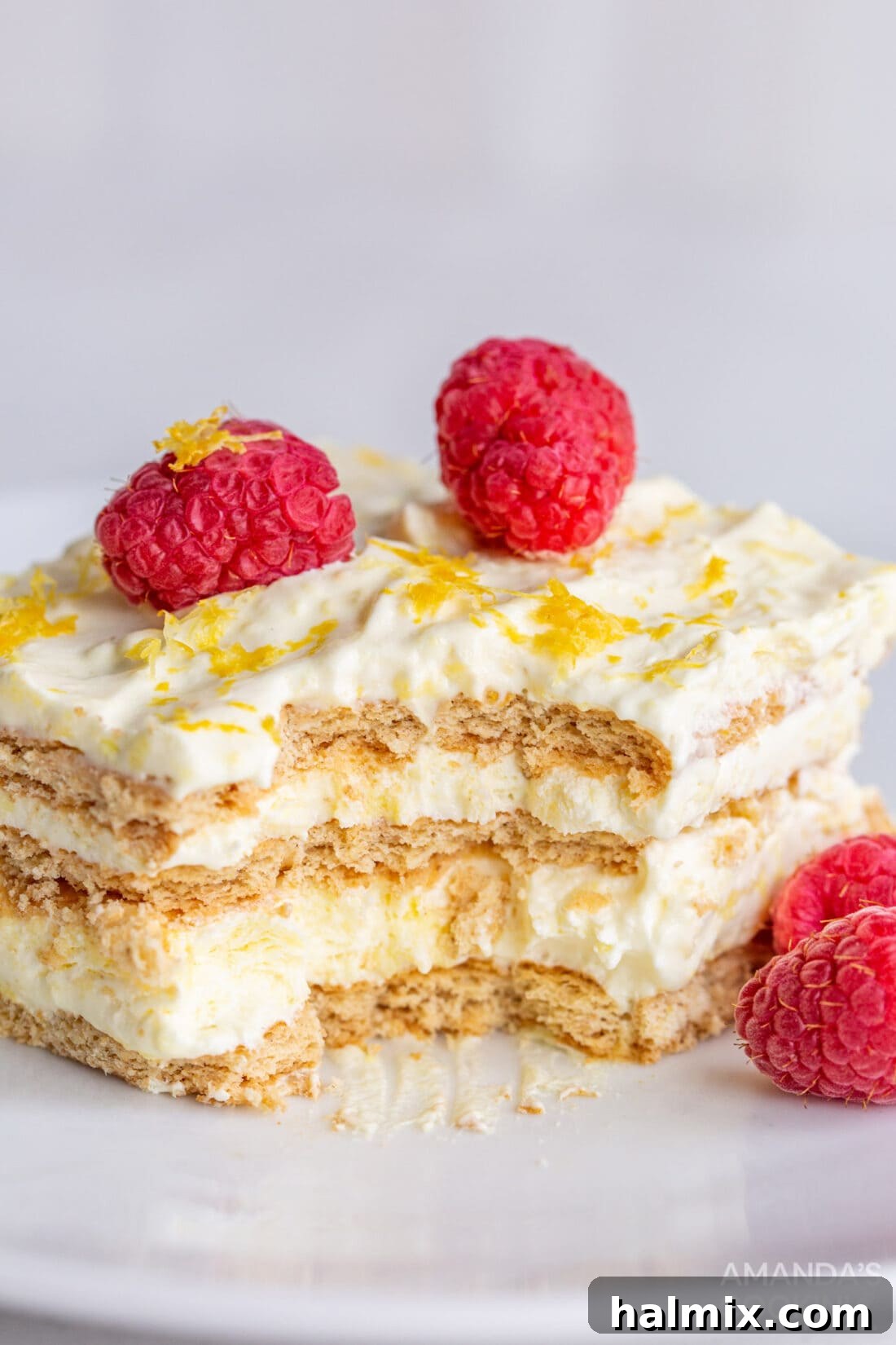 Refreshing Lemon Icebox Cake 3 close-up of lemon icebox cake slice with a few bites taken, revealing the pudding, whipped cream, and graham cracker layers