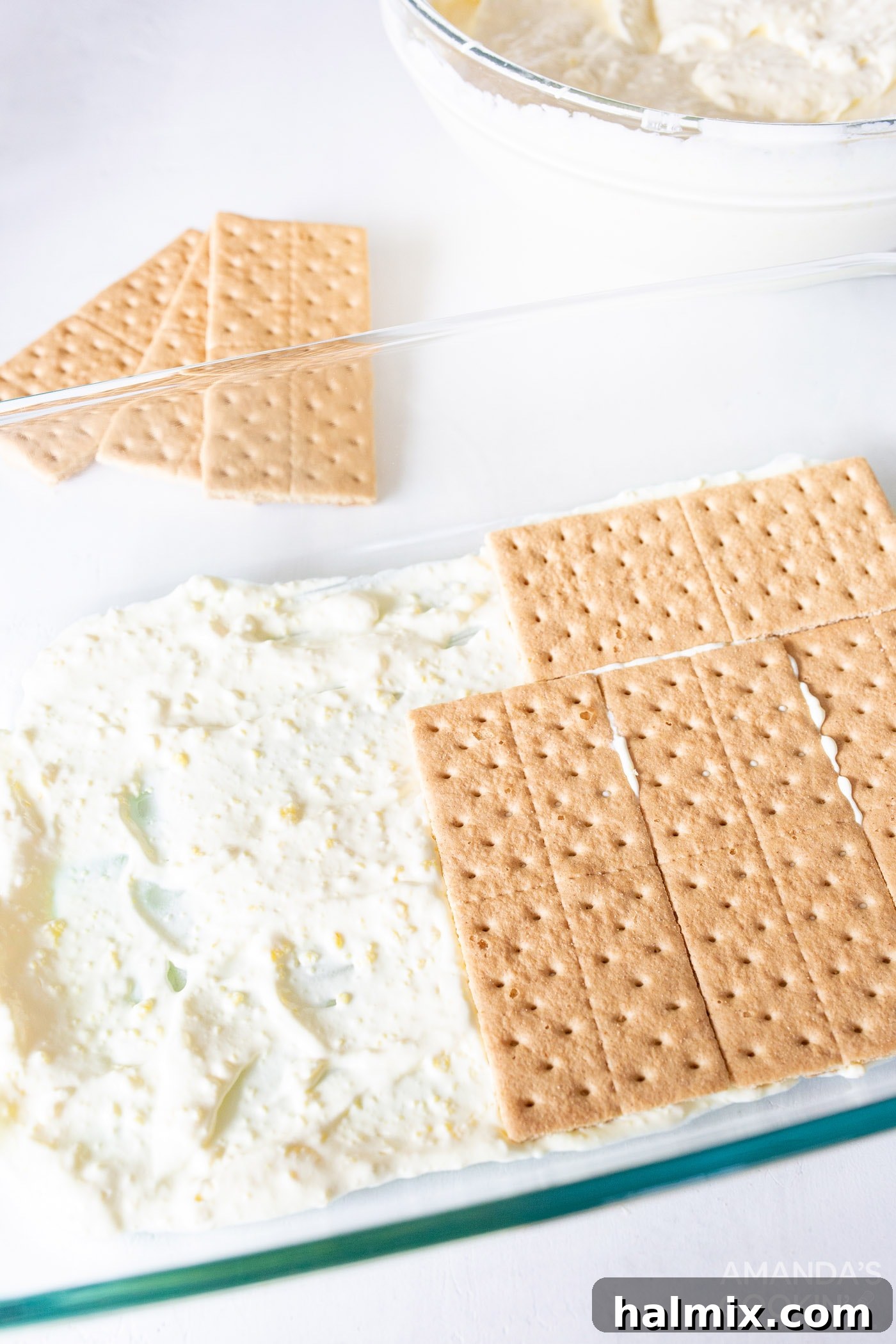 Refreshing Lemon Icebox Cake 9 graham crackers being laid over a thin layer of lemon pudding mixture in a 9x13 baking dish
