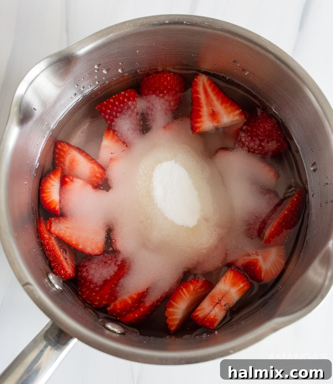 Sliced strawberries, sugar, and water in a saucepan simmering to create simple syrup