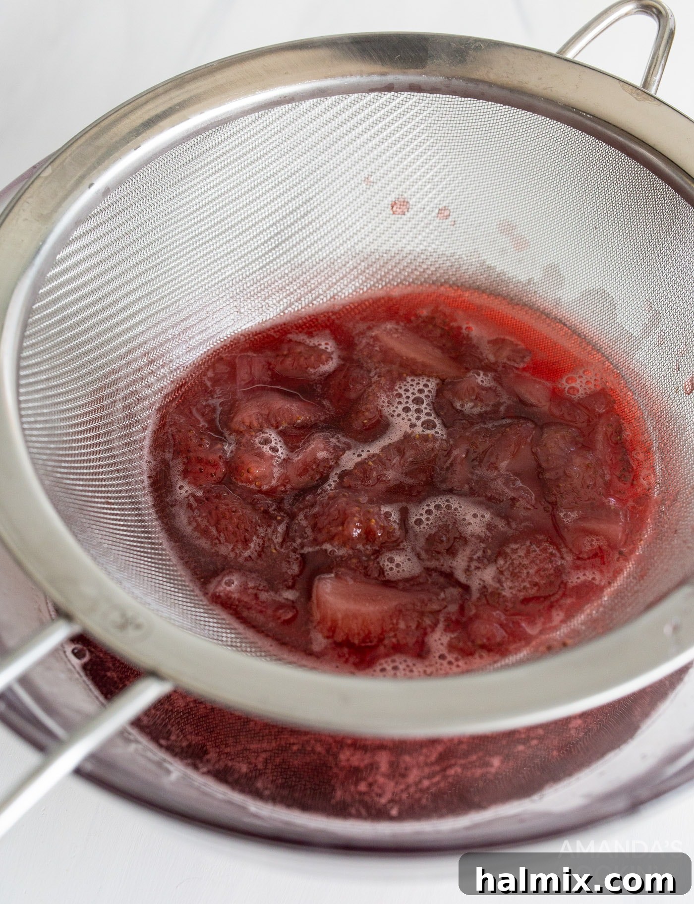Strawberry simple syrup being strained through a fine-mesh strainer into a bowl