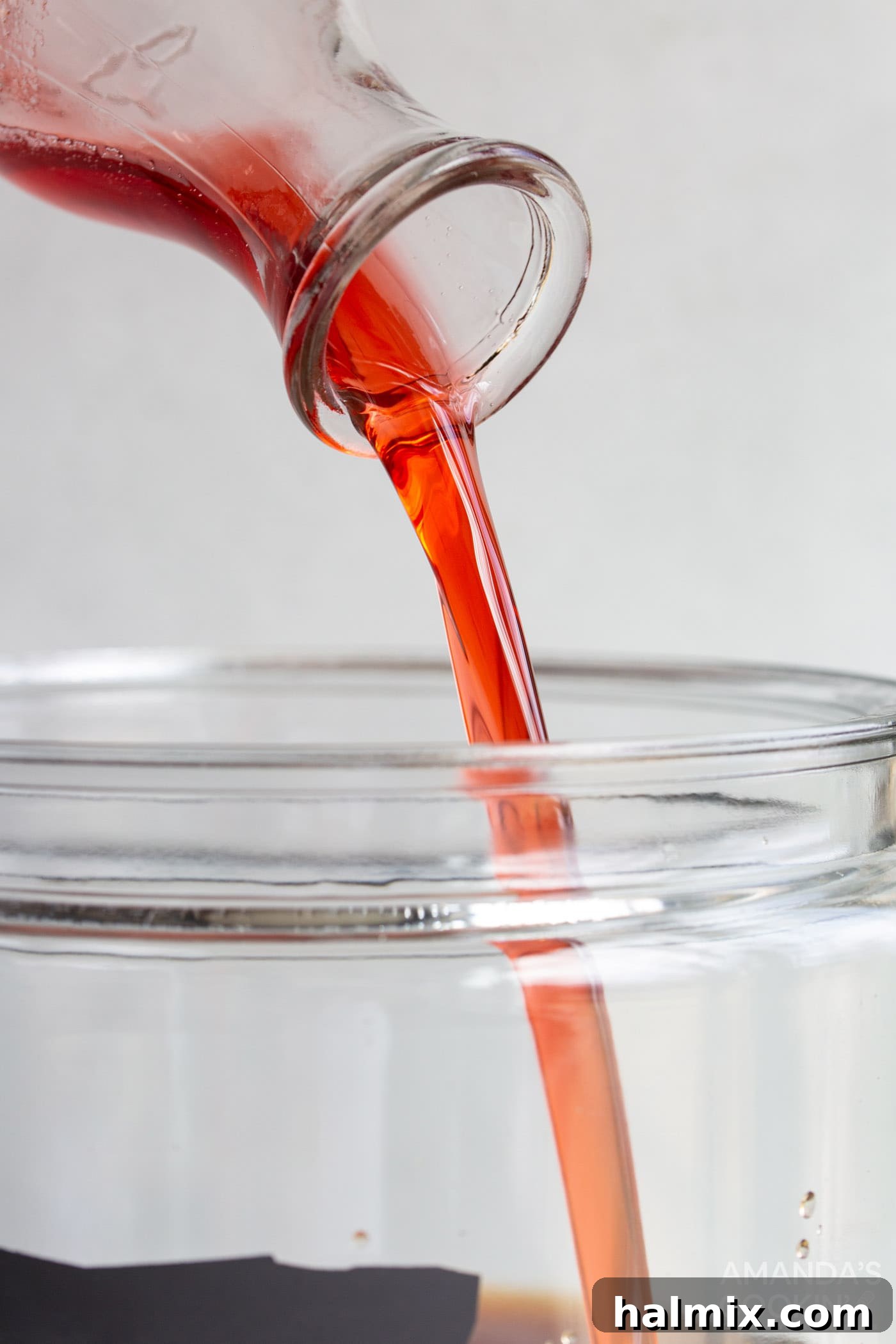Pouring strawberry simple syrup into a pitcher of brewed tea with ice and lemon slices