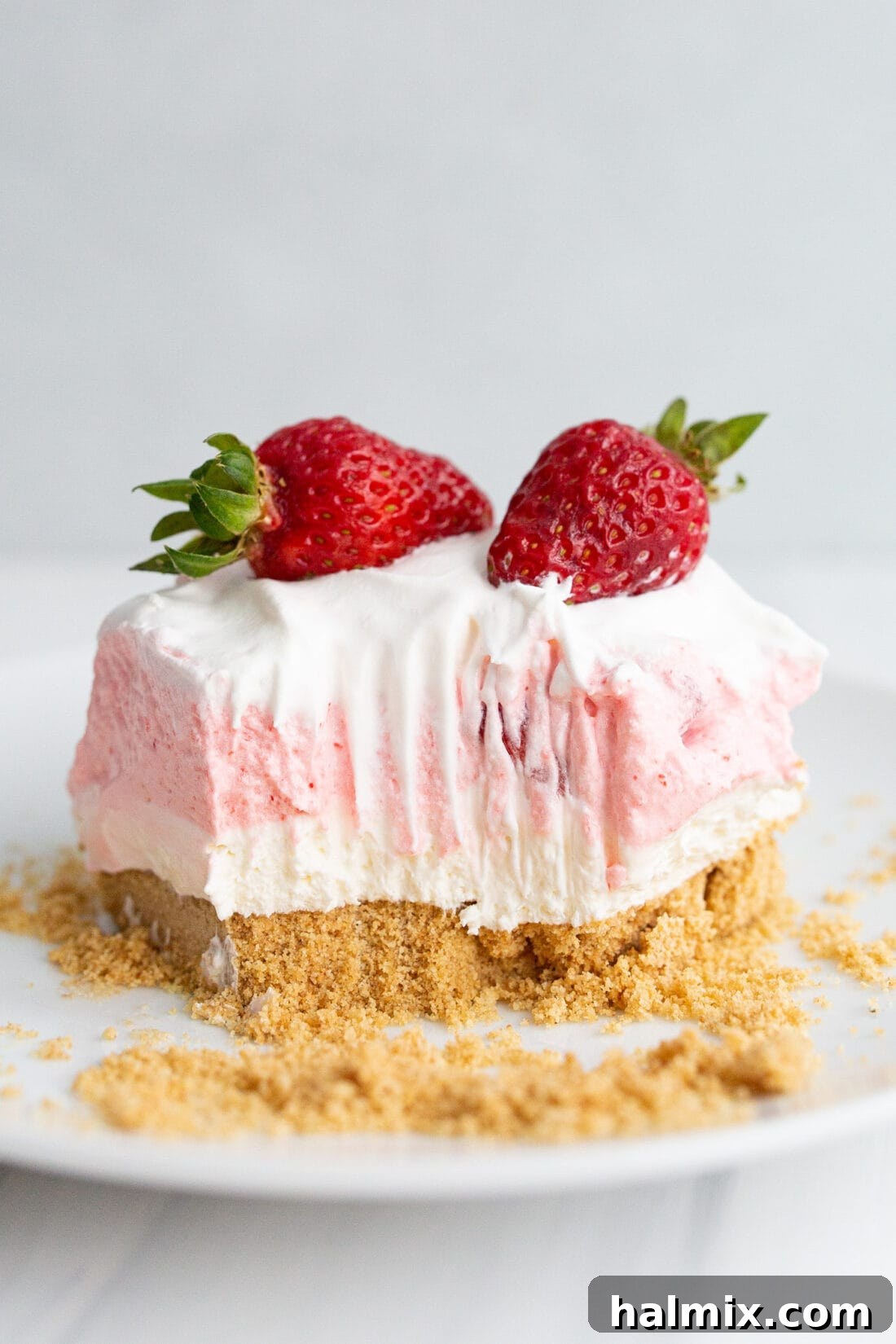 Square of Strawberry Lasagna on a plate with a bite taken out, showing distinct layers of crust, cheesecake, jello with strawberries, and whipped topping.