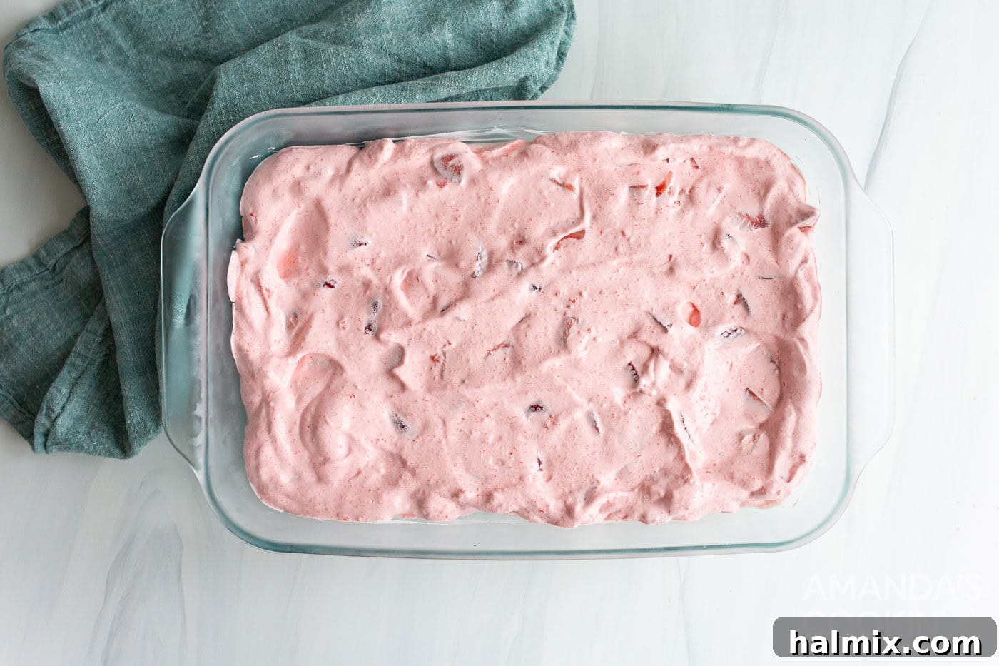The strawberry jello and cool whip mixture spread evenly over the cheesecake layer in the baking dish