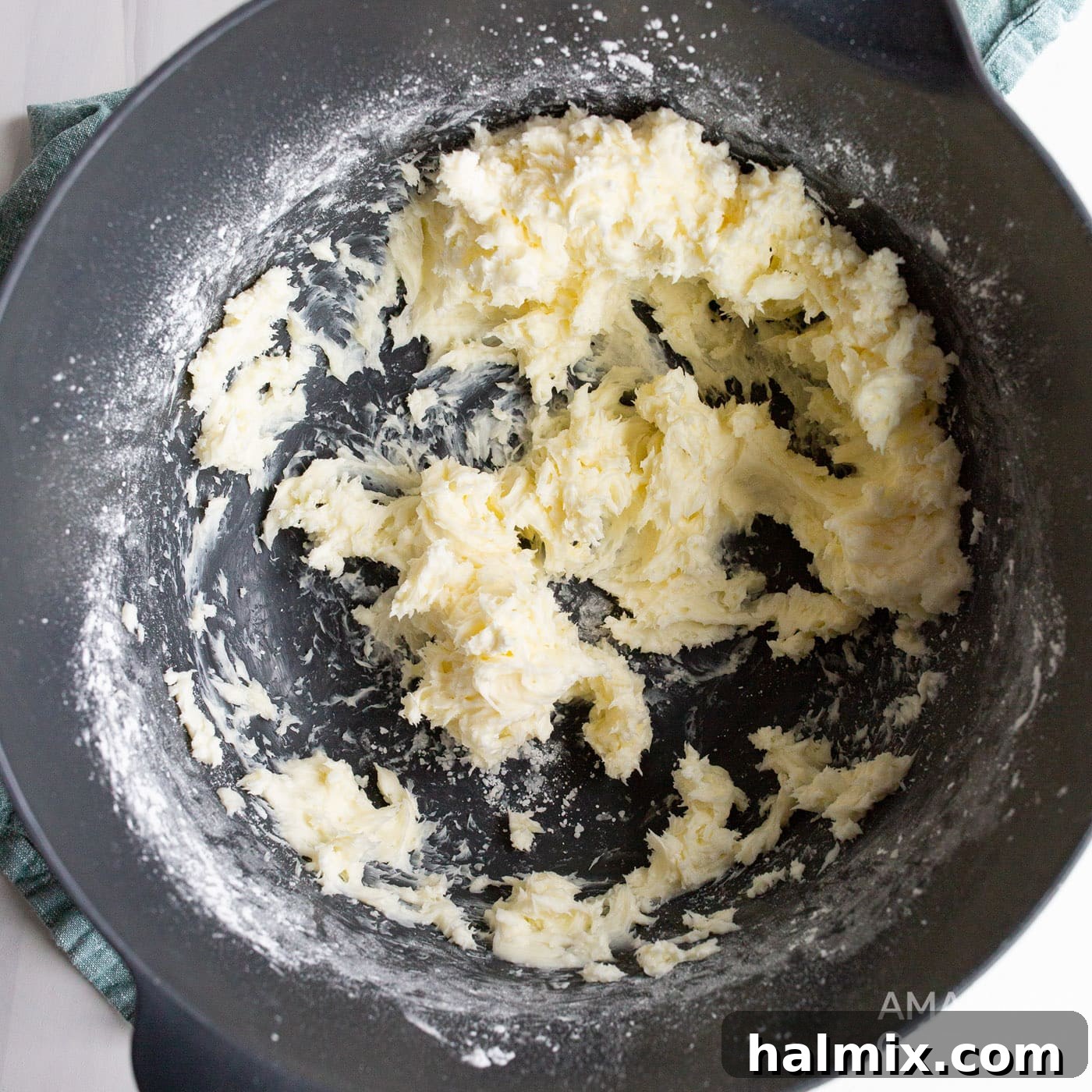 Softened cream cheese being whipped with powdered sugar in a bowl