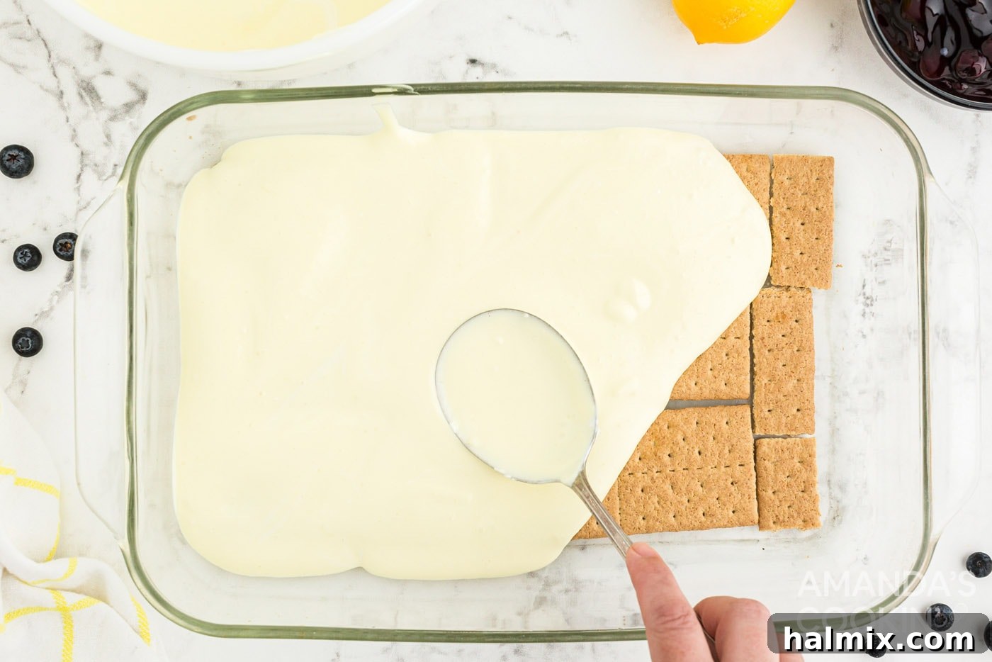 Zesty Lemon Blueberry No-Bake Delight 7 spooning pudding layer over graham crackers in casserole dish