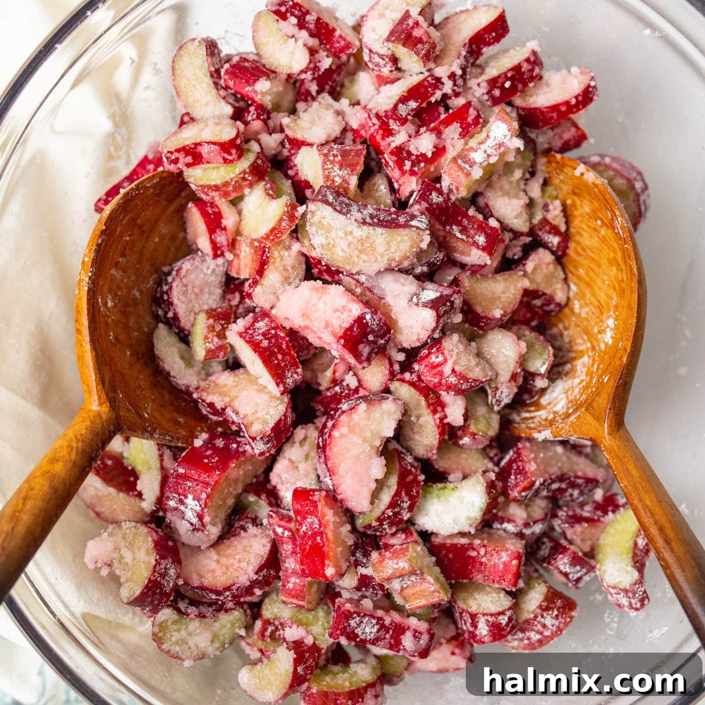 Sweet & Tangy Rhubarb Crunch 5 A bowl filled with chopped rhubarb mixture, lemon juice, sugar, and cornstarch, with two wooden spoons for mixing