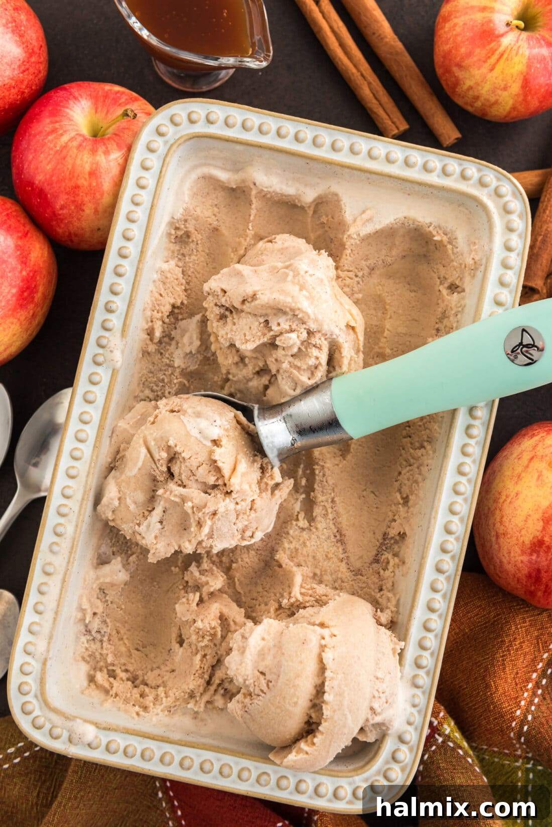A pan filled with freshly made apple cider ice cream, with an ice cream scoop poised, ready to serve. The creamy texture and inviting color are prominently displayed, hinting at its deliciousness.