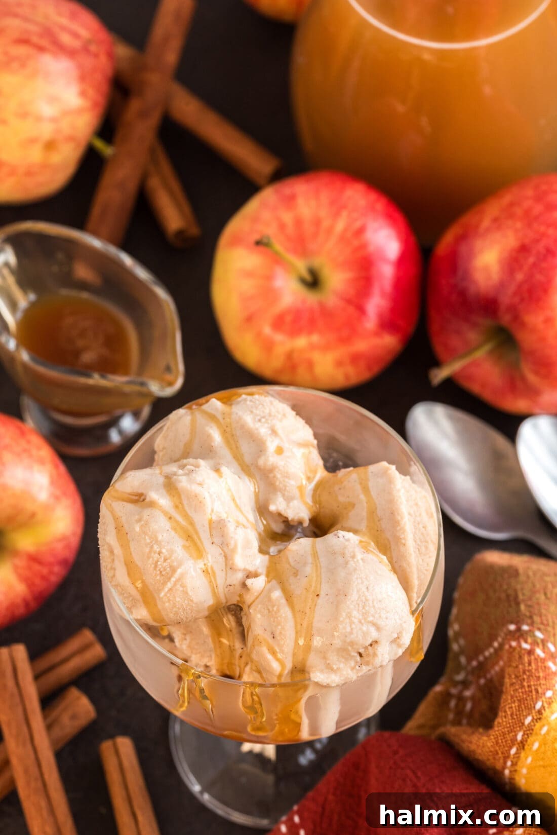 Three perfect scoops of rich Apple Cider Ice Cream nestled in a clear glass dish, beautifully adorned with a generous swirl of golden caramel drizzle, ready to be enjoyed.