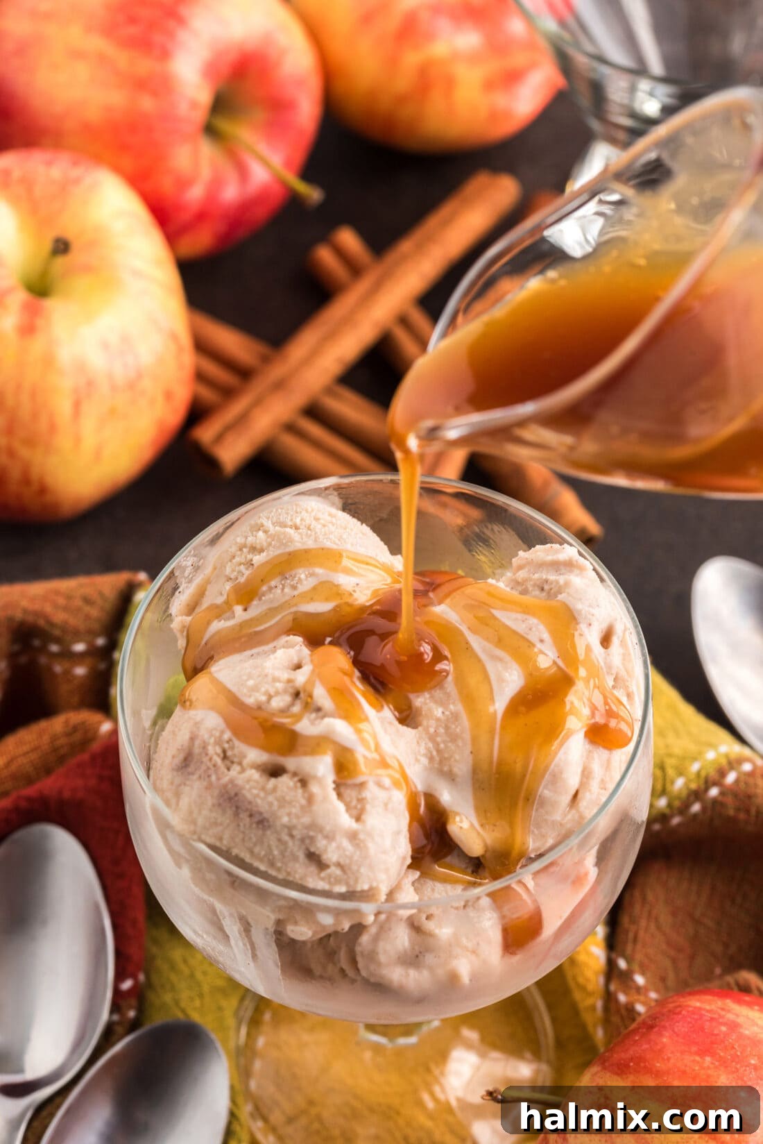 Golden caramel sauce artfully drizzled over two generous scoops of creamy Apple Cider Ice Cream, presented in an elegant glass dish. The glistening caramel promises an added layer of sweetness and luxury.