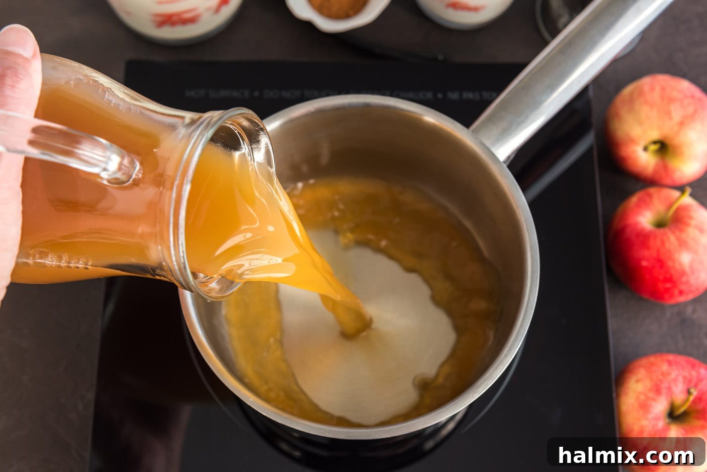 Pouring a stream of fresh apple cider from a bottle into a stainless steel saucepan, beginning the preparation for the ice cream base.