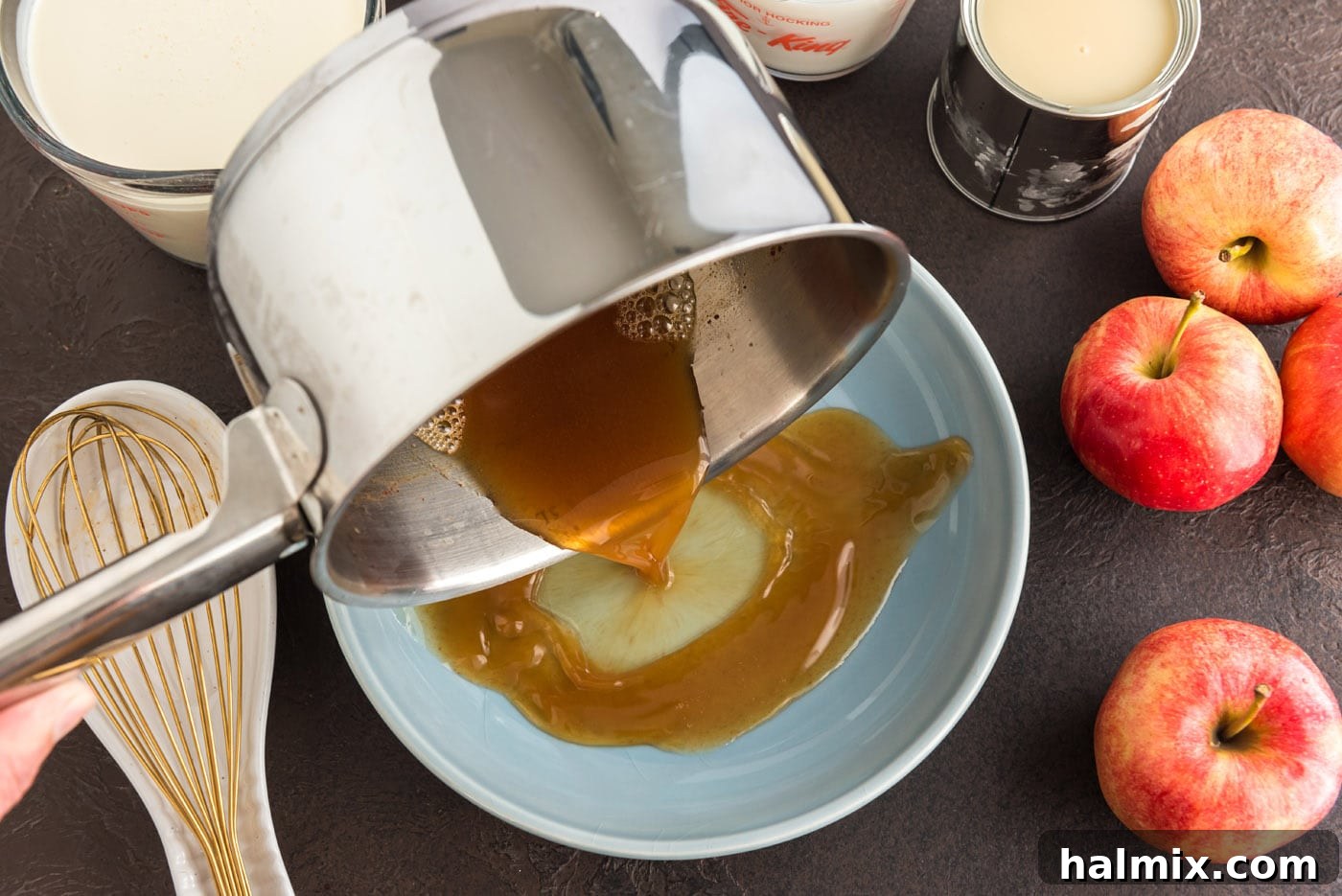 The concentrated, hot apple cider being carefully poured from a saucepan onto a wide, flat white plate to facilitate quick cooling. Steam is visible rising from the liquid.