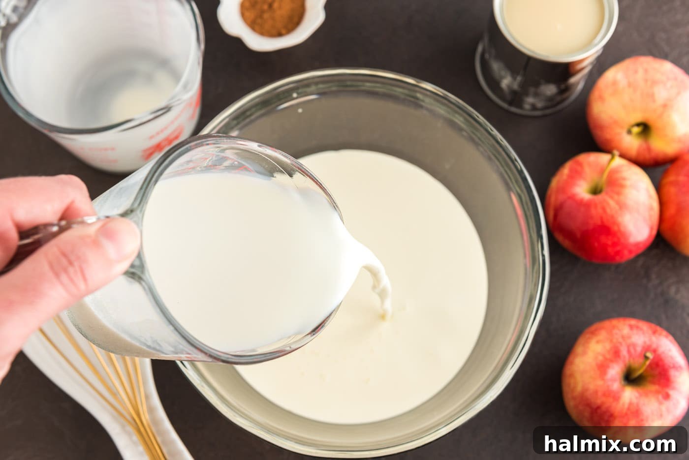 A stream of thick heavy cream being poured from a carton into a large glass mixing bowl, signaling the start of the ice cream base preparation.
