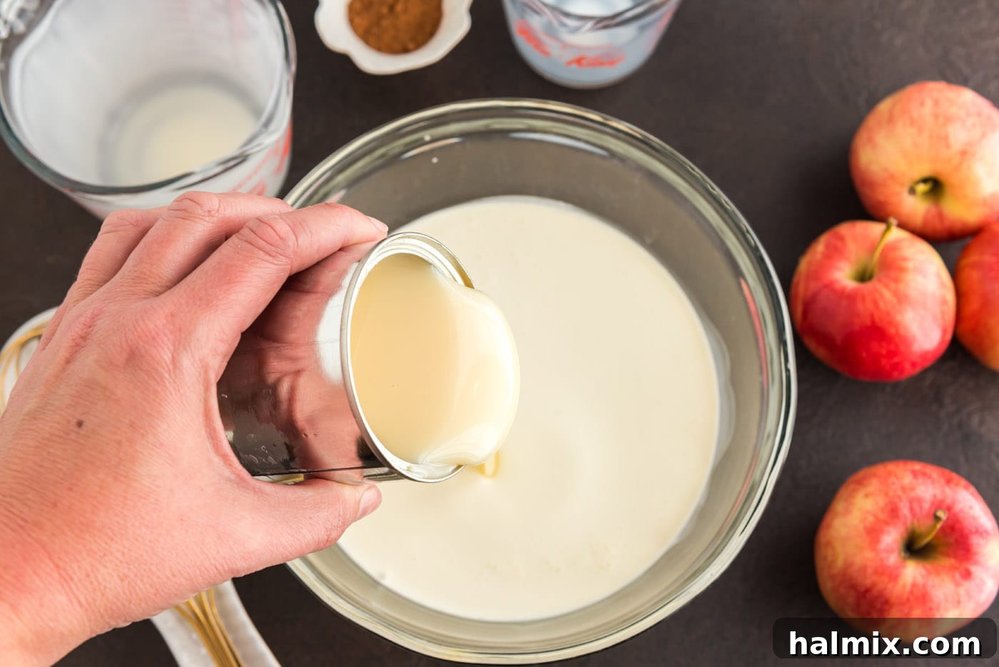 Sweetened condensed milk being poured from its can into a large mixing bowl that already contains heavy cream. This combination is essential for the ice cream's sweetness and texture.