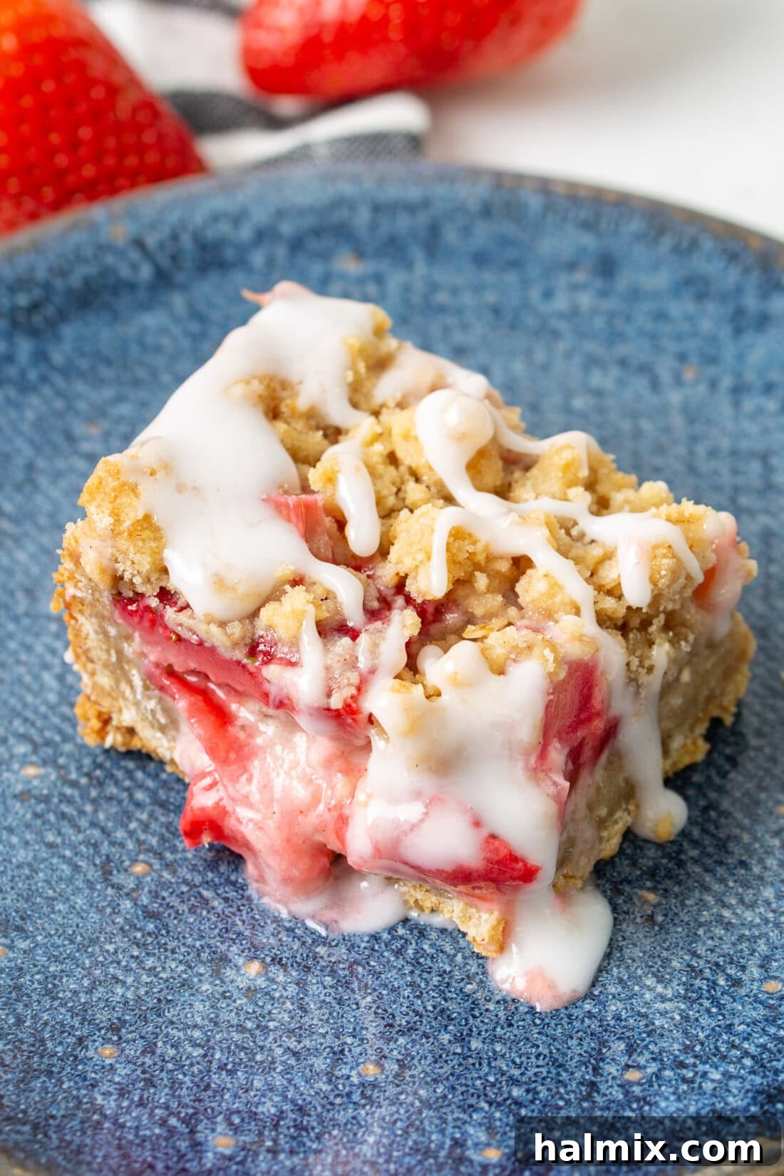 Close-up photo of a single Strawberry Rhubarb Crumble Bar on a blue plate, highlighting the crumbly texture, juicy fruit layers, and a hint of icing drizzle