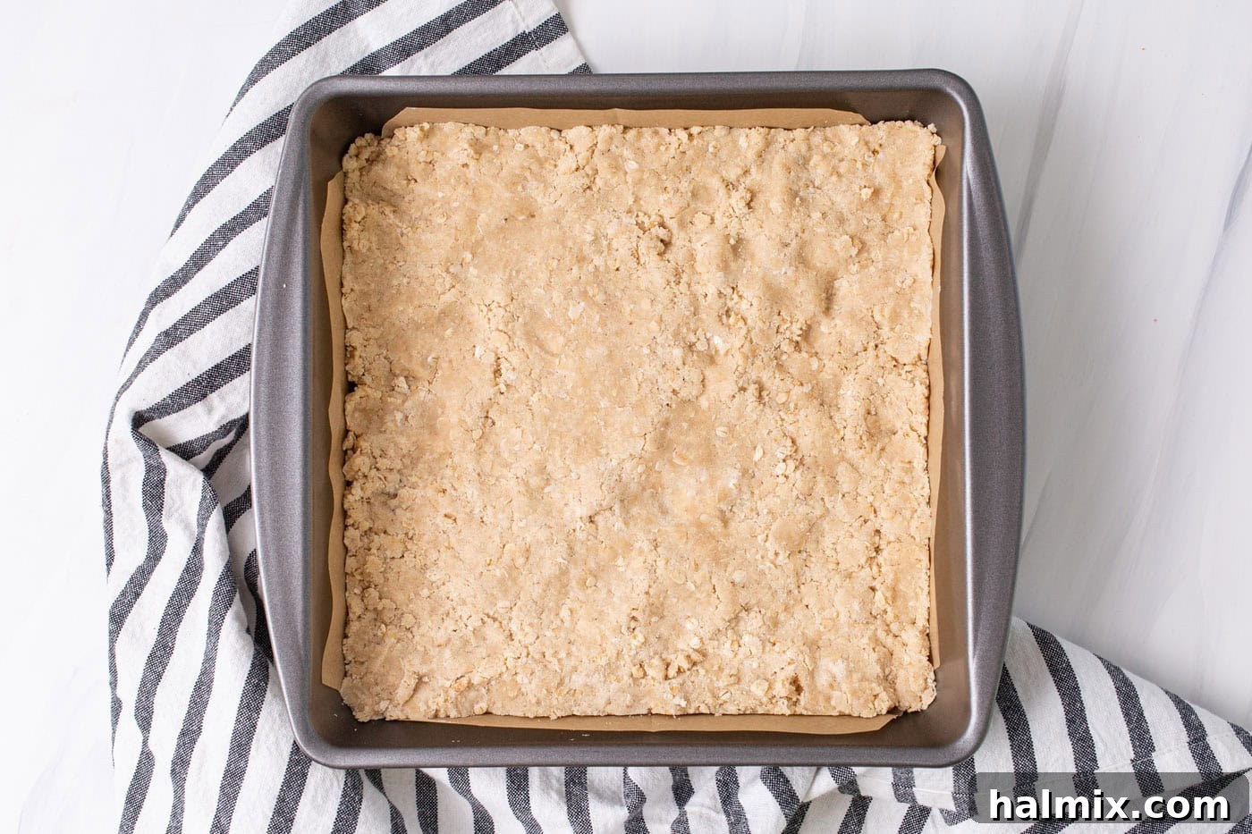 The base crust of rhubarb crumble bars, made from pressed crumble mixture, set firmly into a parchment-lined baking pan